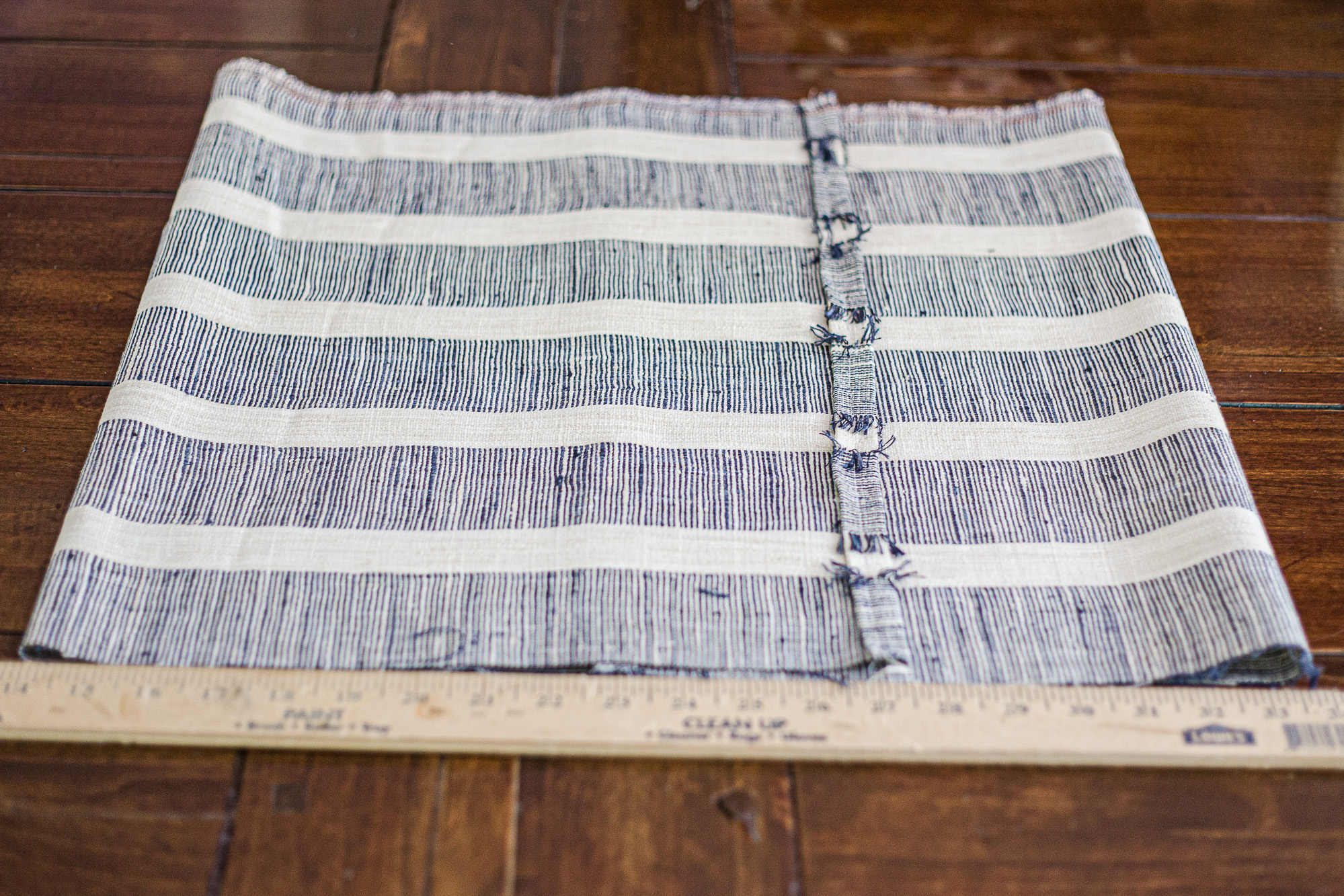 Folded blue and white stripe fabric laying on a table with wooden measuring stick