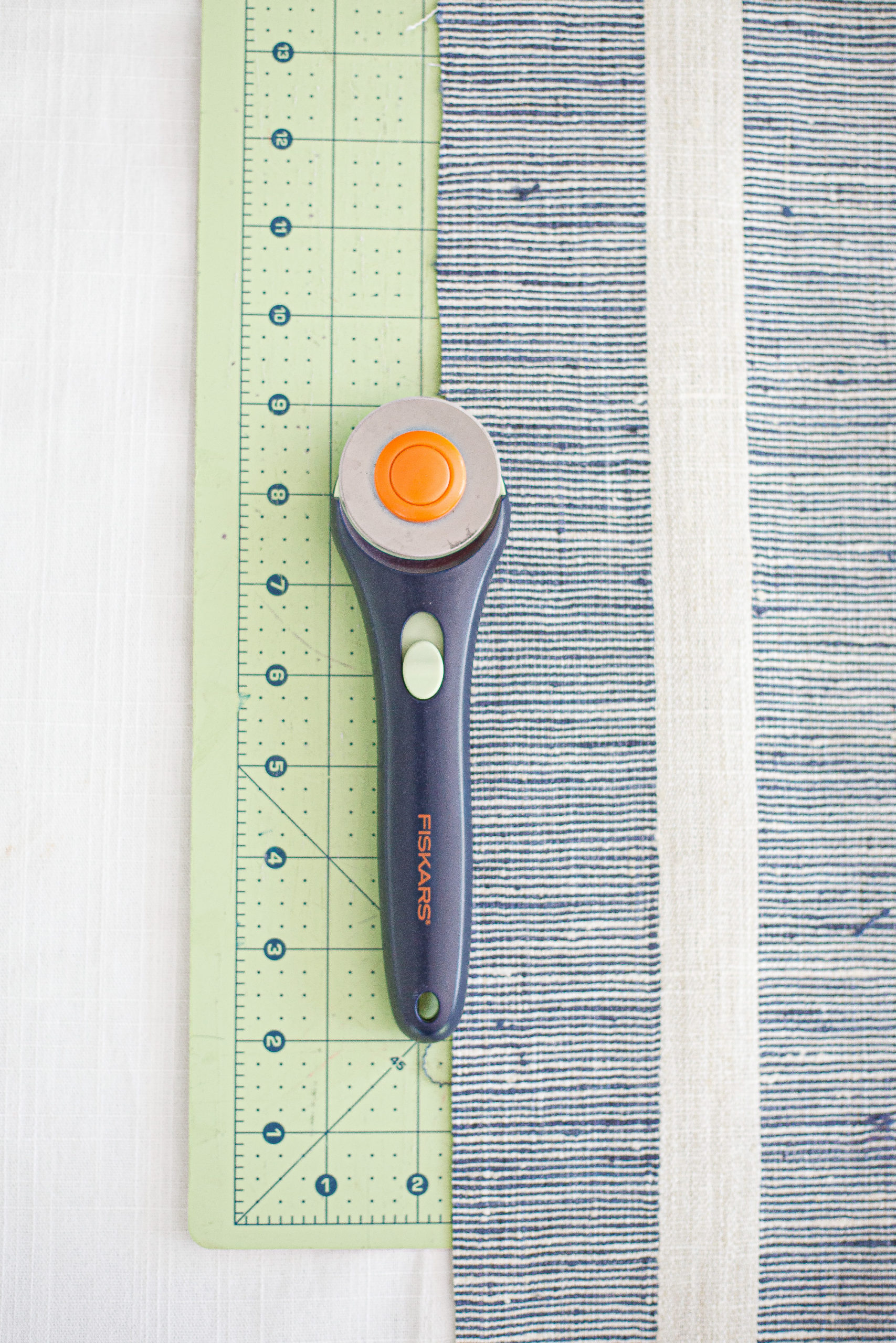 blue stripe fabric laying on a table with rotary cutter sitting on top with measuring stick