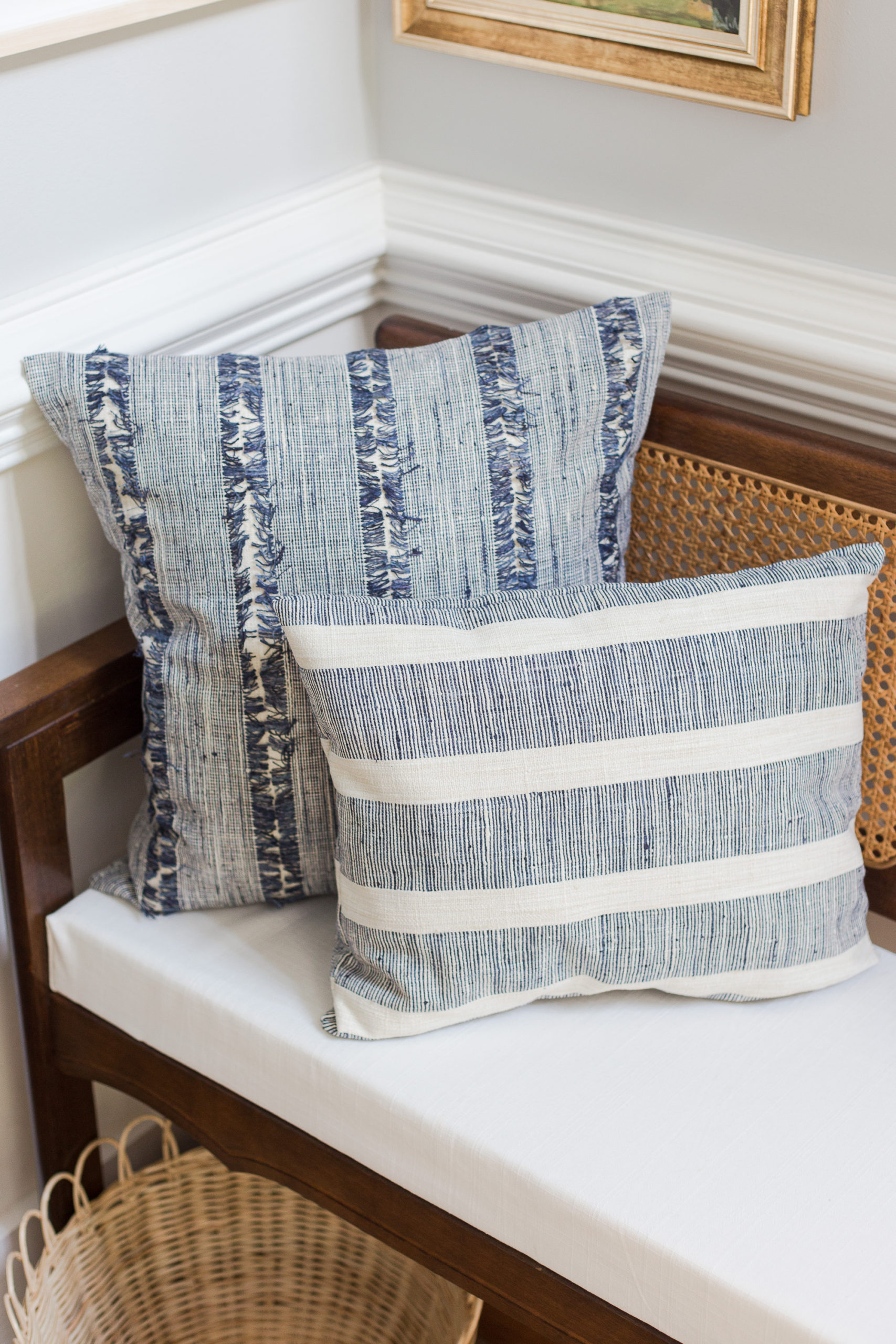 two Blue and white stripe pillows sitting on a cane bench