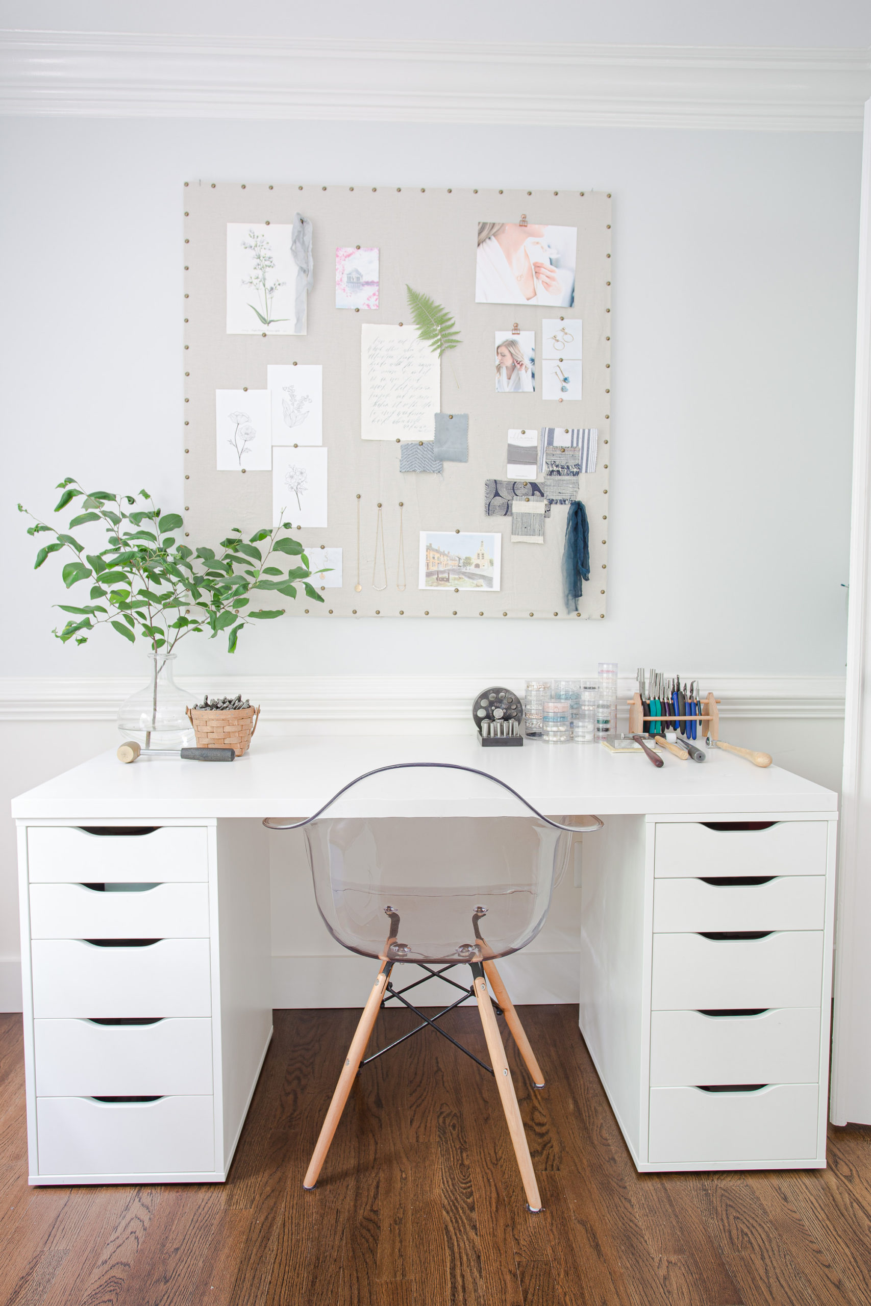 home office jewelry studio desk with white desk, clear chair and vase of green branches