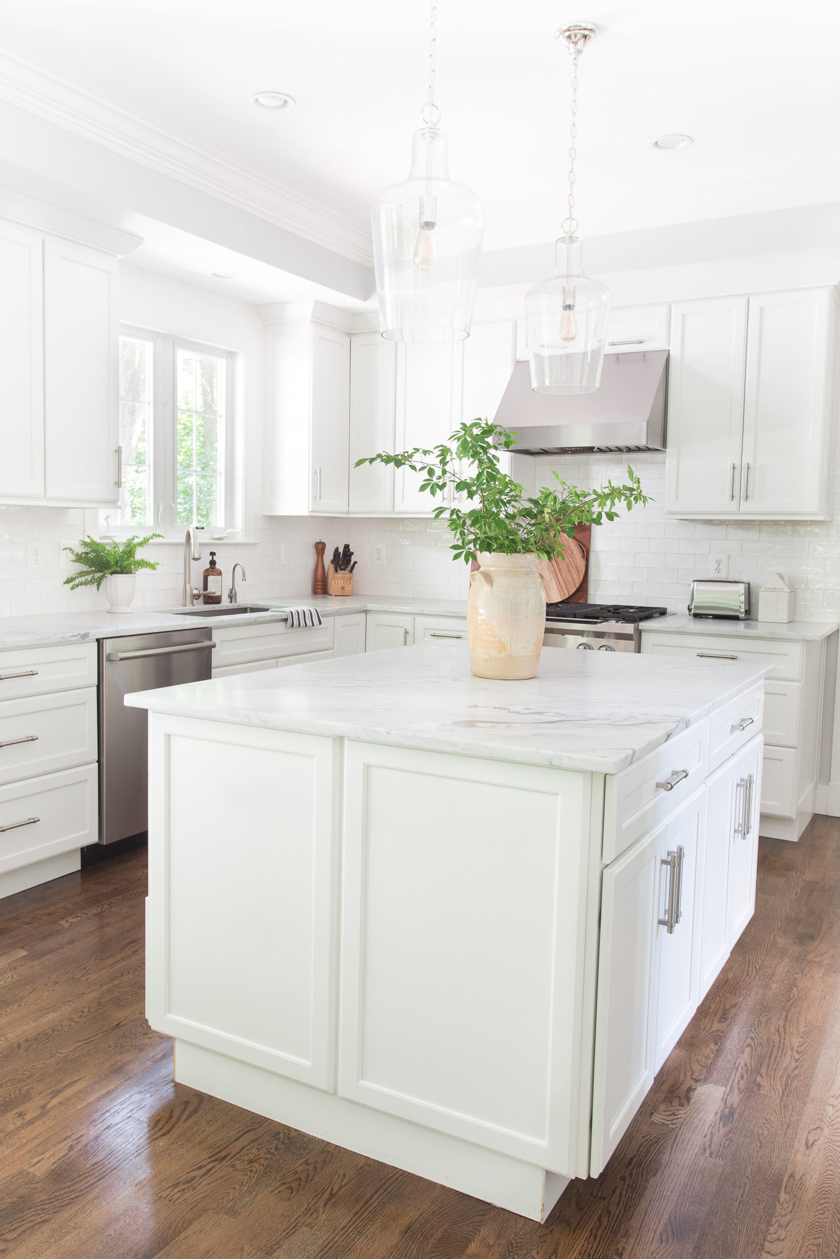 white kitchen with island and marble kitchen countertops with antique vase and greenery