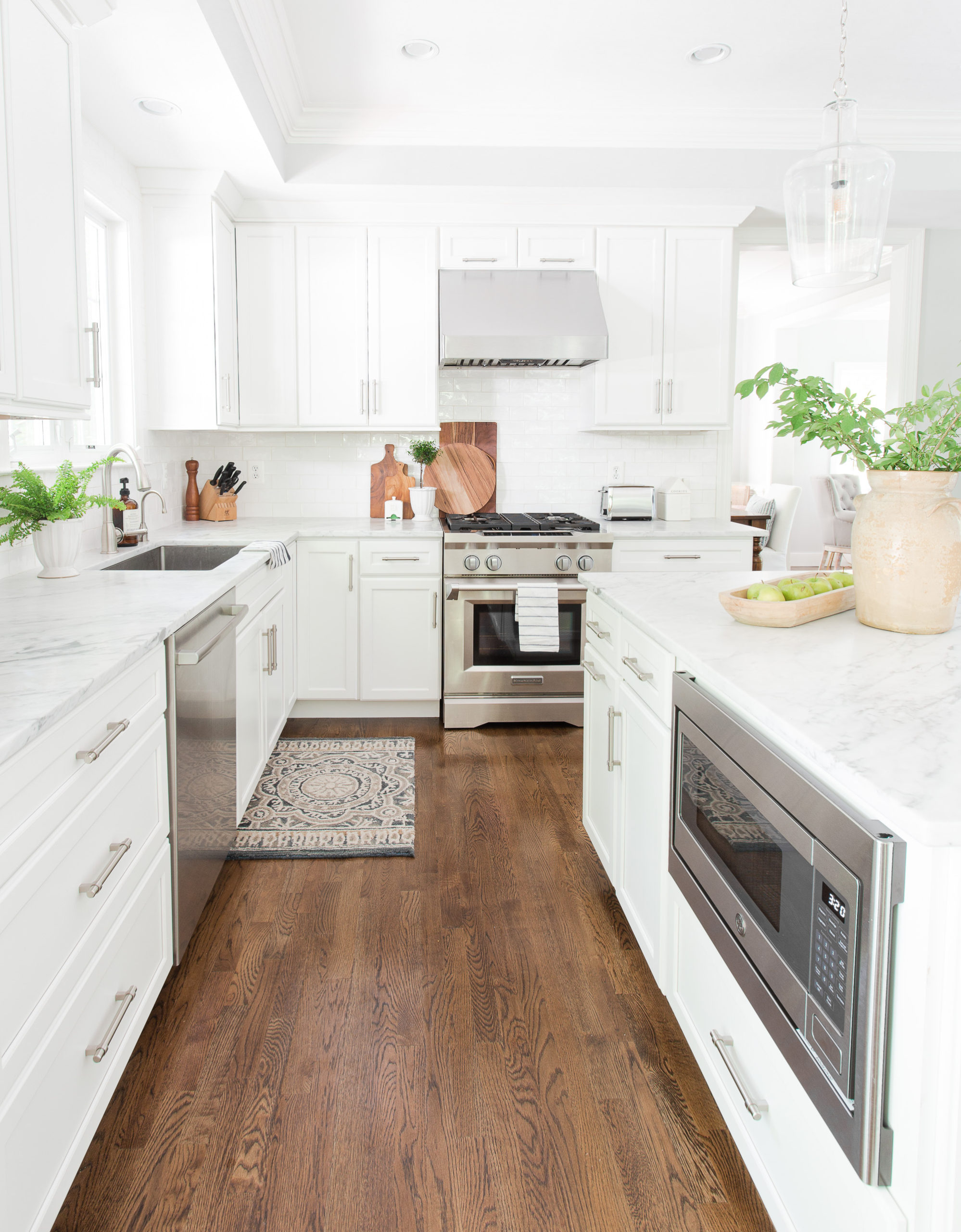 white kitchen with wood floors, gas range, microwave in island and vase of greenery on island countertop