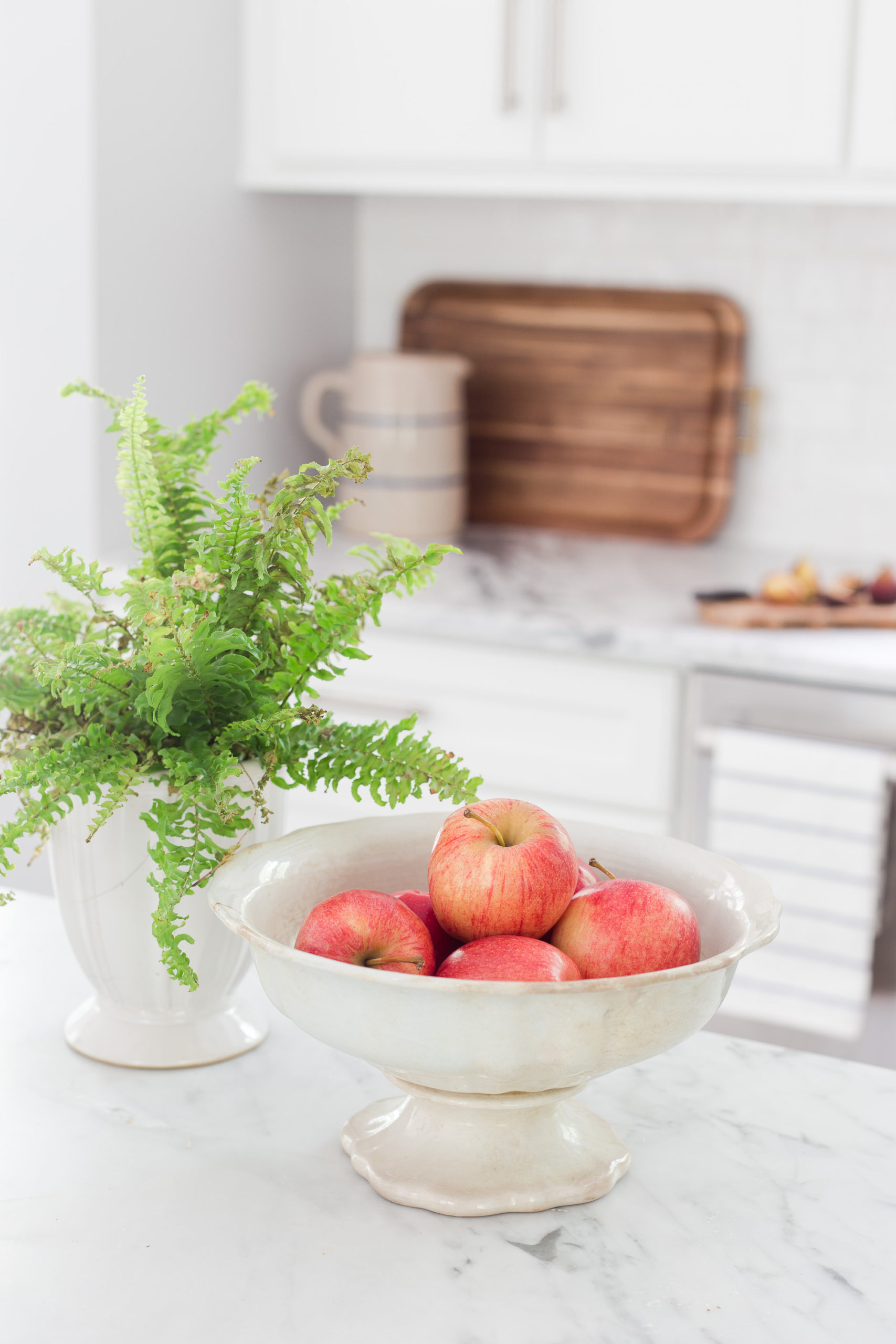 bowl of apples with a fern sitting next to it sitting on a marble kitchen countertop