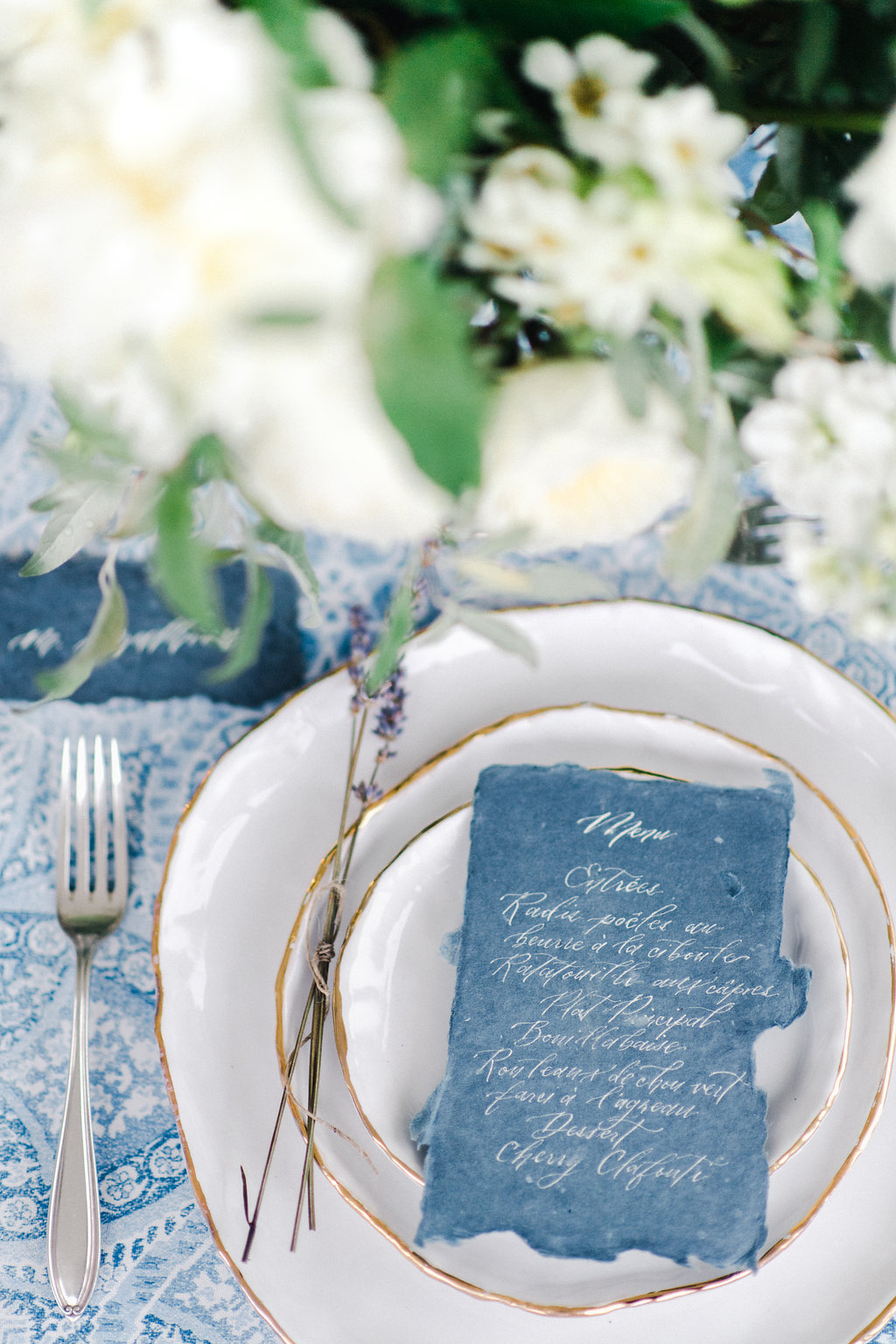 blue hand calligraphy menu card sitting on top of white plates with gold trim