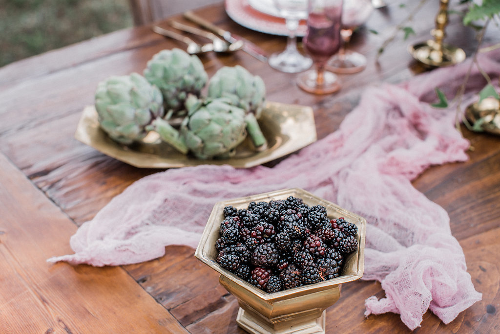table with brass bowl of blackberries and tray of artichokes. 