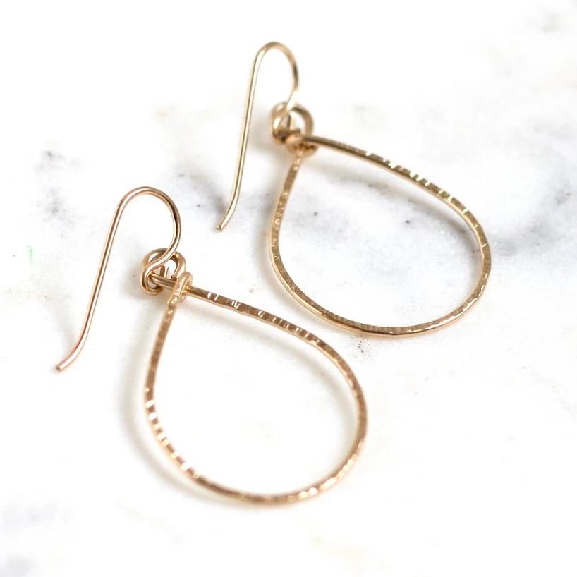 hammered gold oval hoop earrings laid out on marble