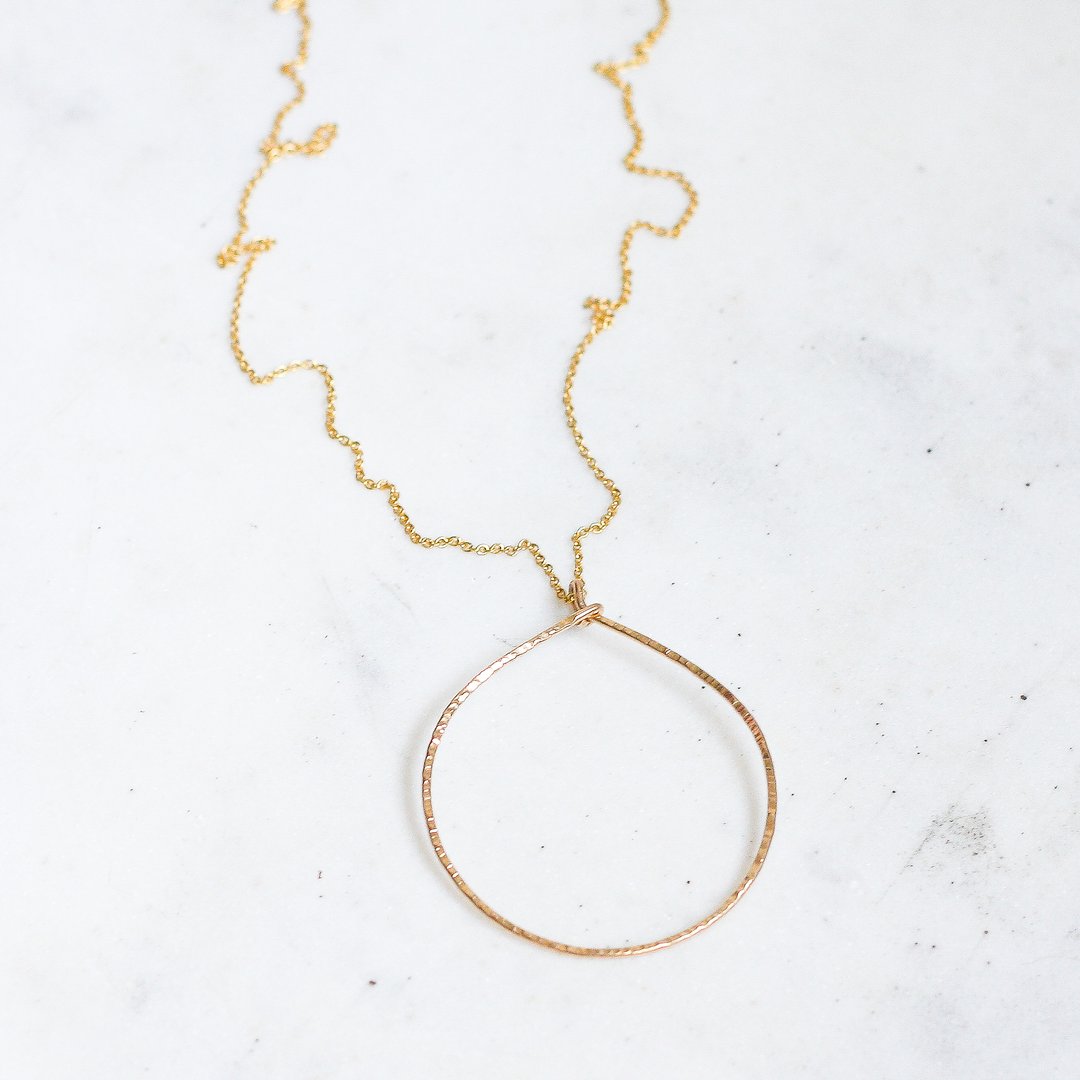 long gold circle necklace laid out on marble