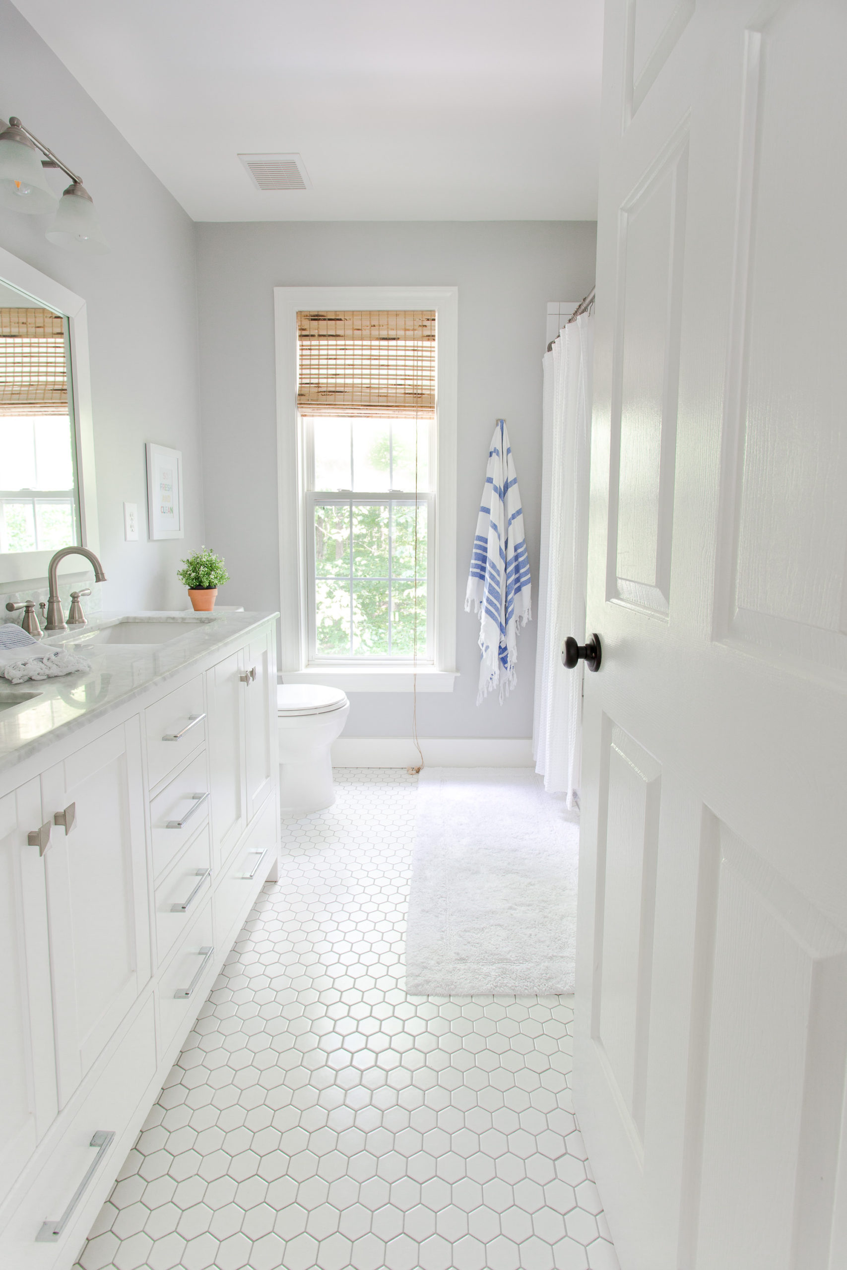 Door open to white bathroom with gray walls, cabinet with two sinks and a blue and white stripe towel hanging on the wall
