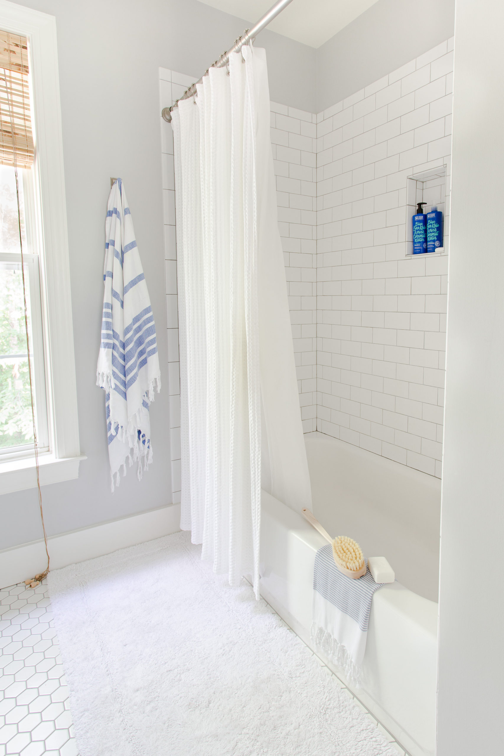 Bath and tub with white subway tile and gray grout with blue and white stripe towel hanging on the wall. 