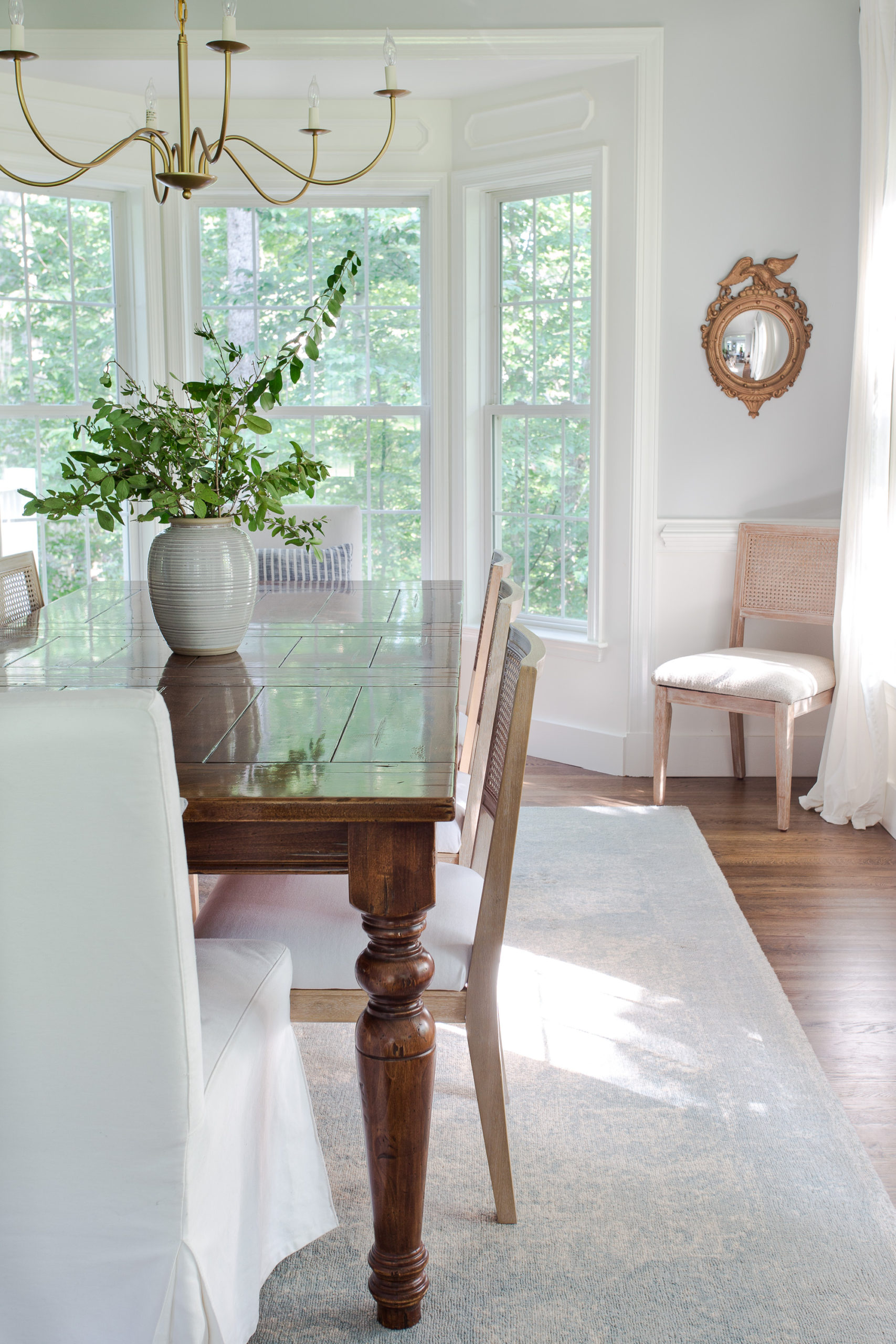 dining room table with chairs on rug with vase of greenery sitting on table and bay window in background