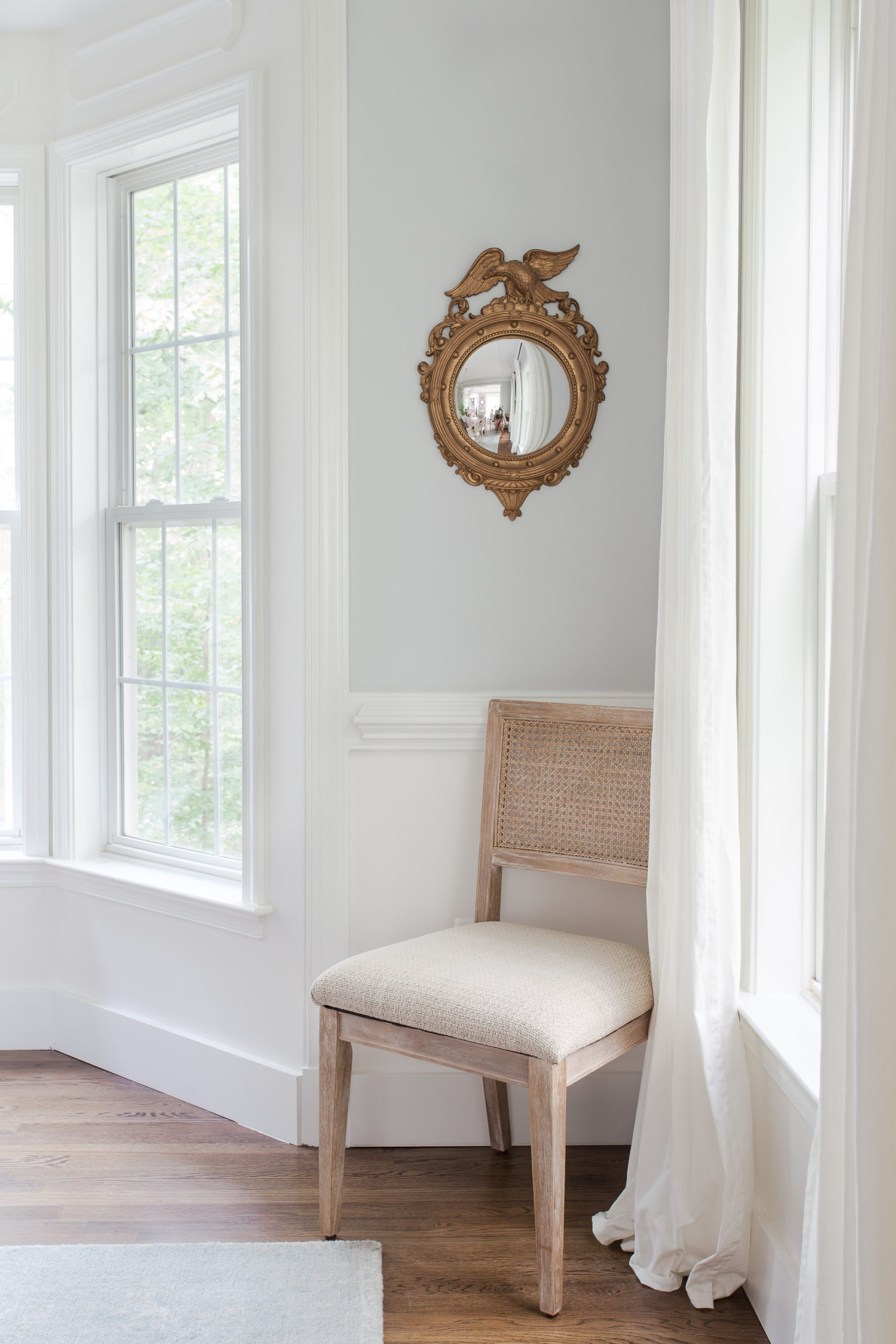 Light wood cane chair sitting in corner of dining room with round gold mirror hanging on wall above chair