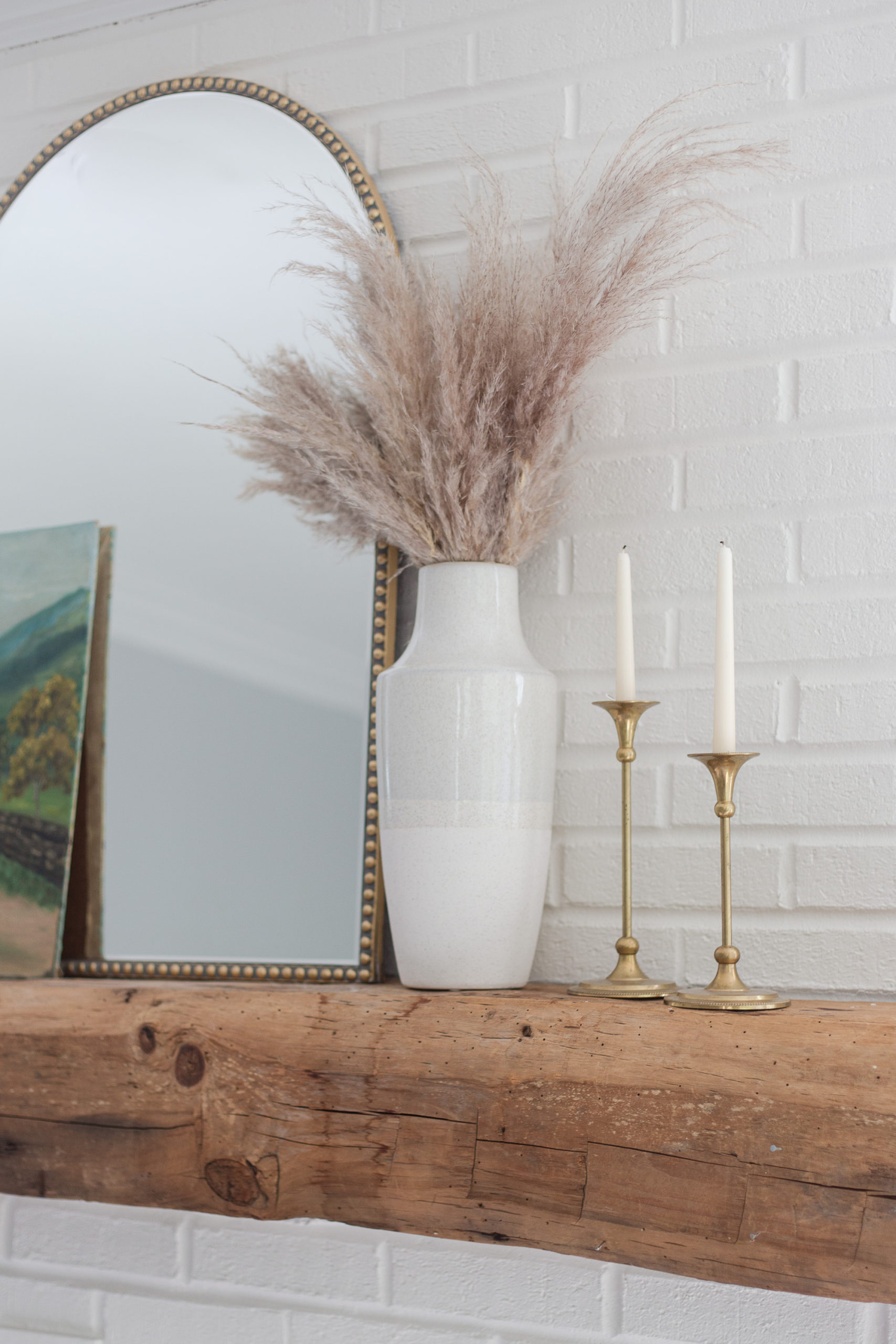 wood fireplace mantel with white brick, brass candlesticks and vase with grass