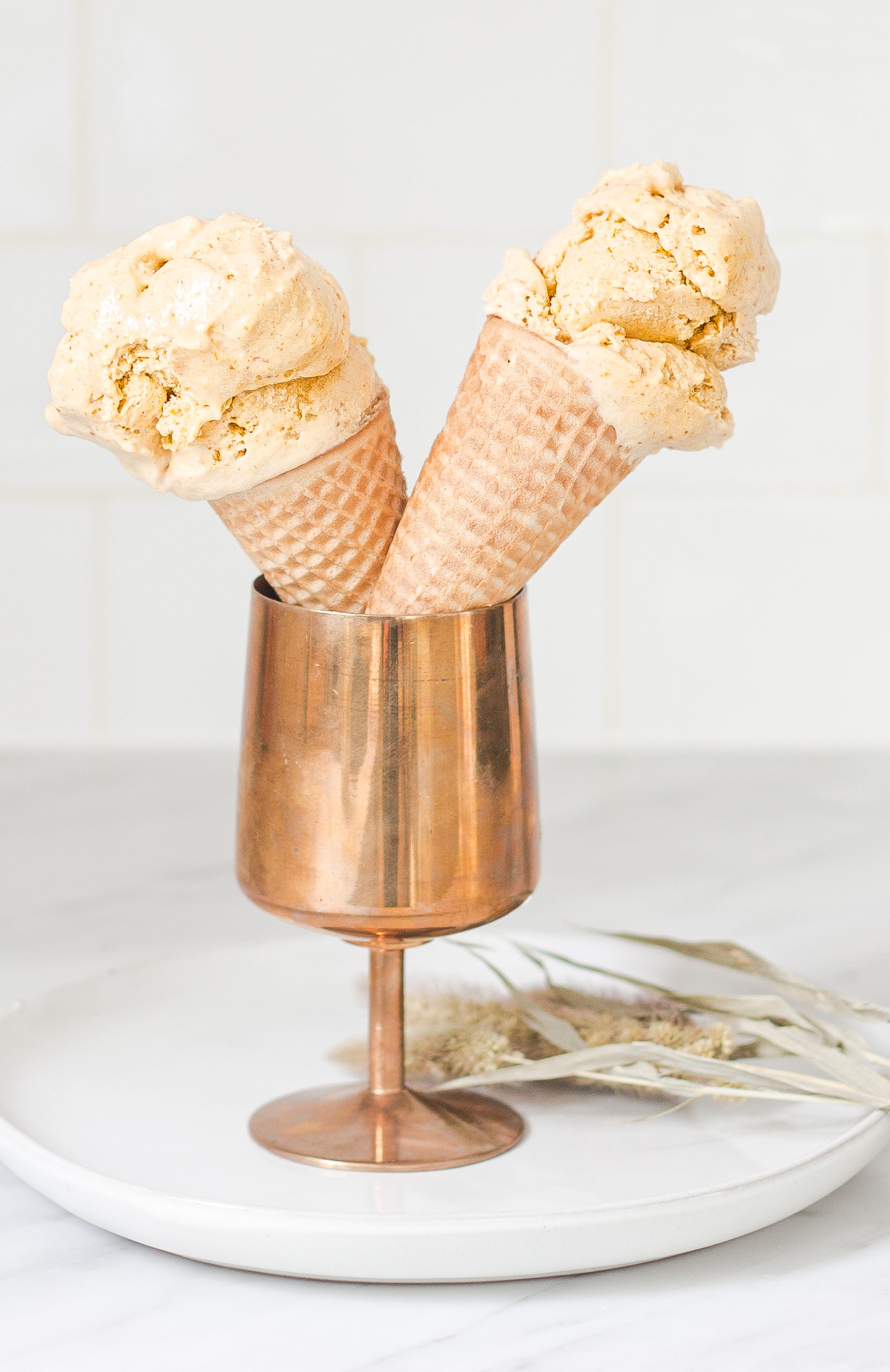 two ice cream cones propped in a copper goblet with scoops of peanut butter ice cream