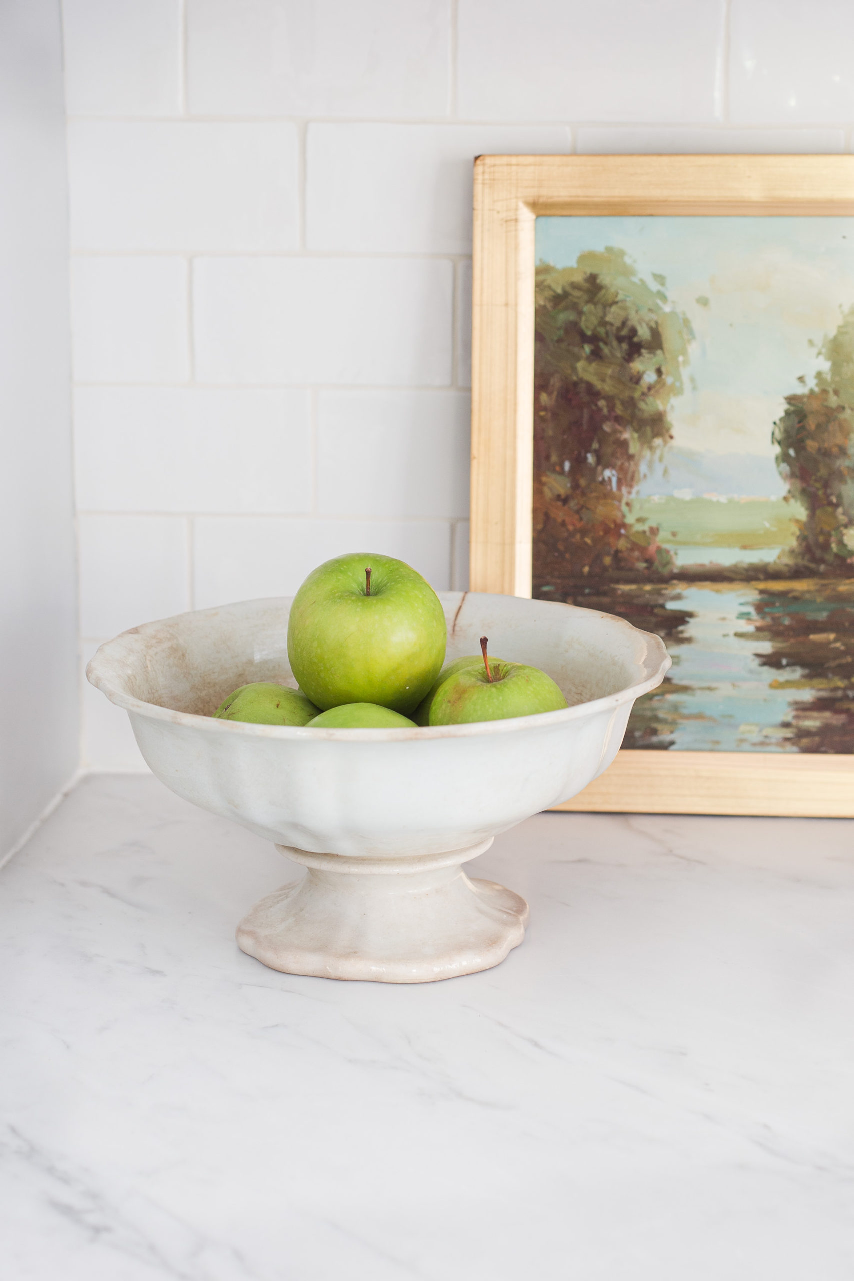 white kitchen countertops with ceramic bow filled with green apples. 