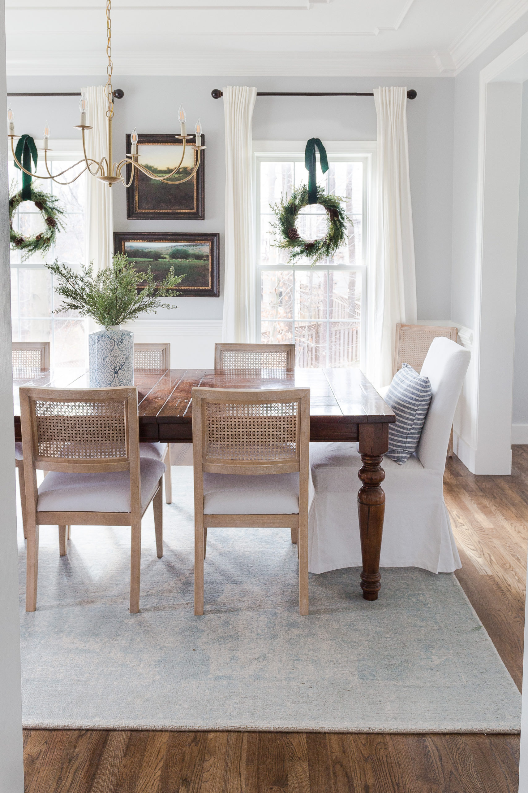 dining room with wooden table and can chair and christmas wreaths hanging in the windows. 