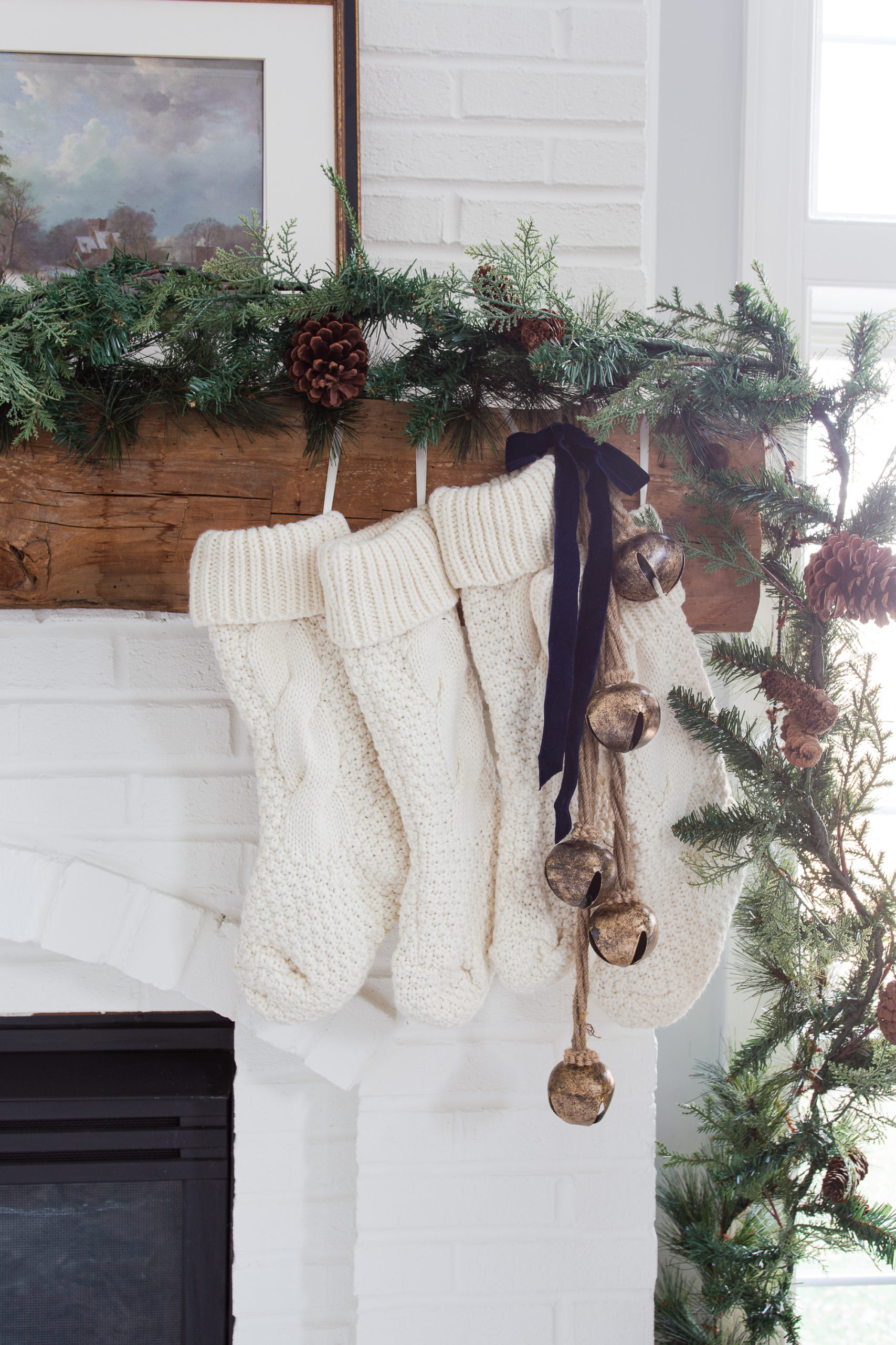 brass bells hanging with stockings from fireplace with green pine garland