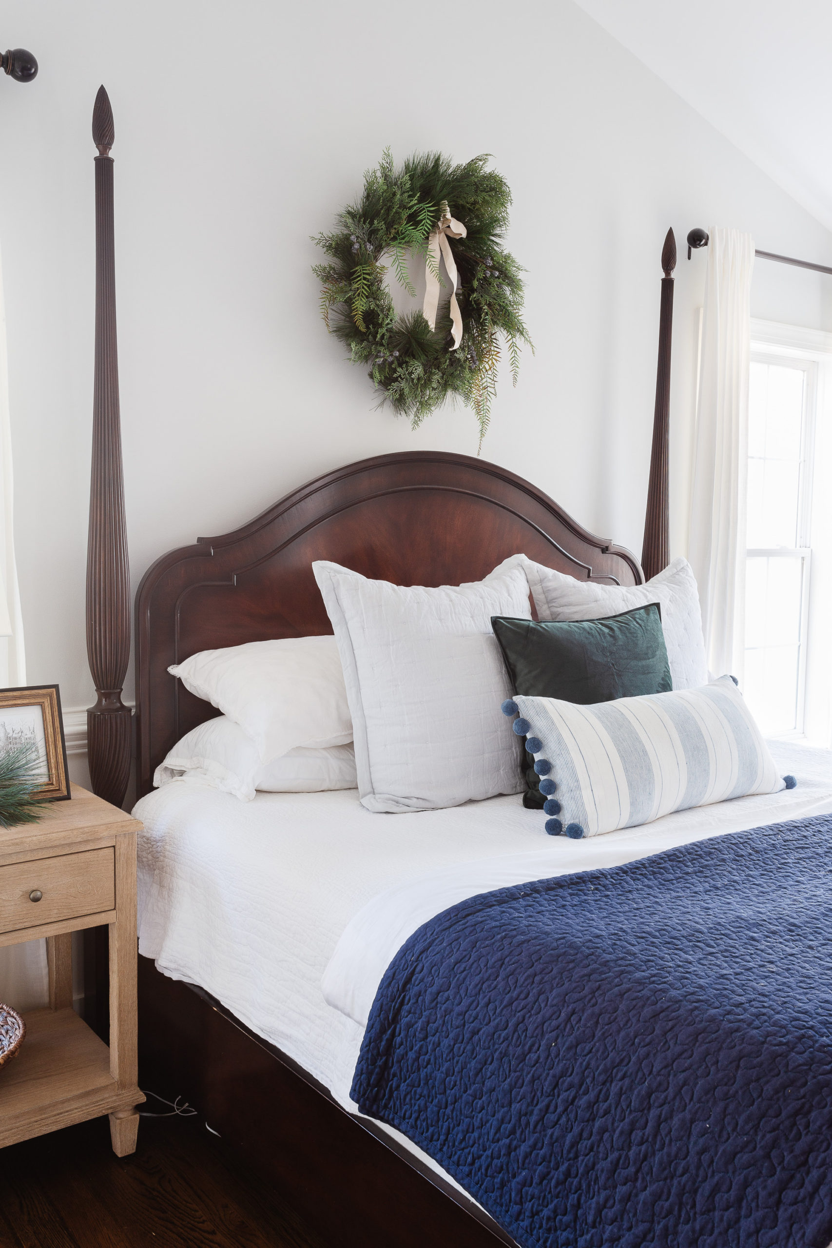 Poster bed with blue quilt and wreath on wall in bedroom