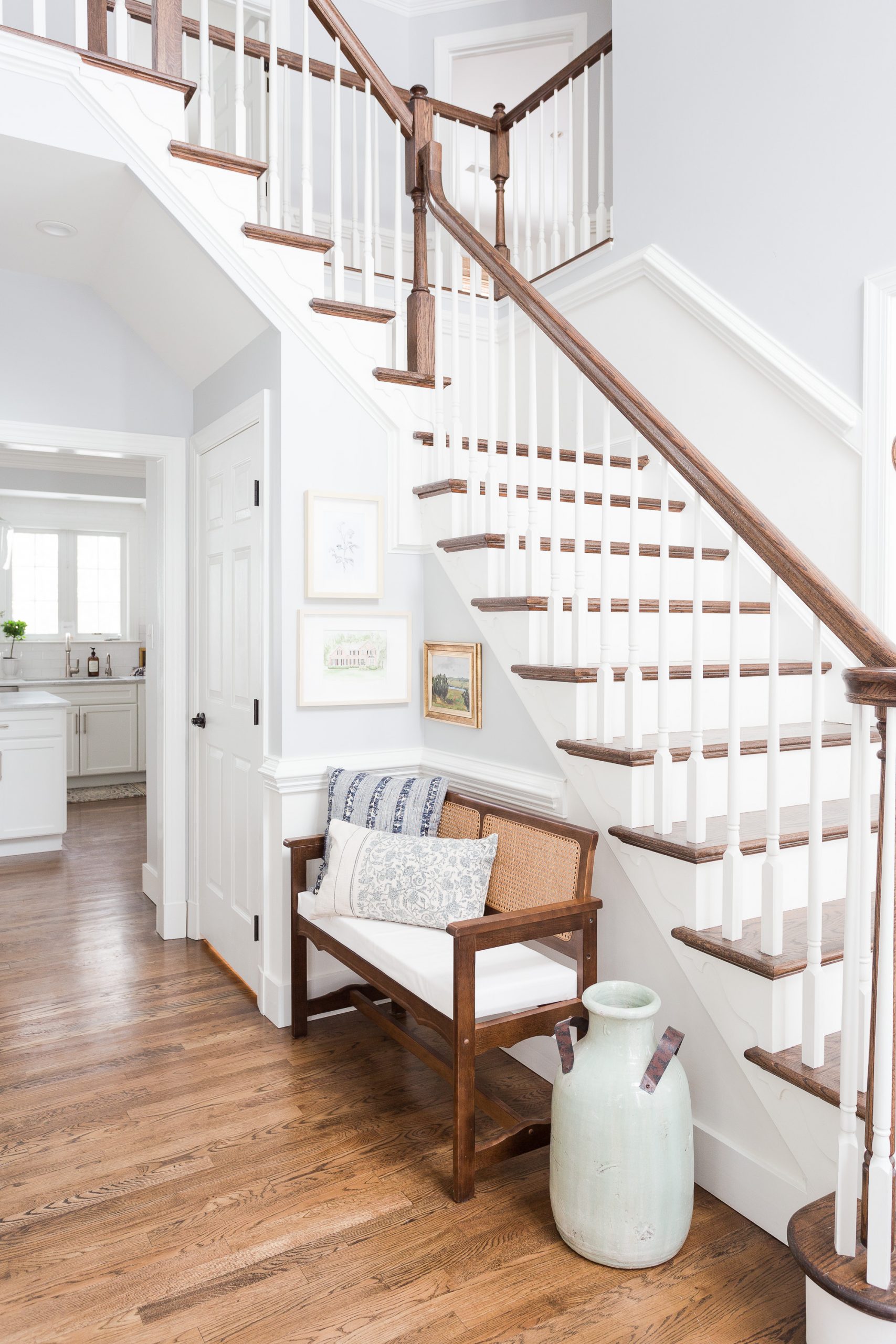 Two story entryway with wood floors and wood step stair case with cane bench in the hallway. Walls and trim are painted White Dove. 