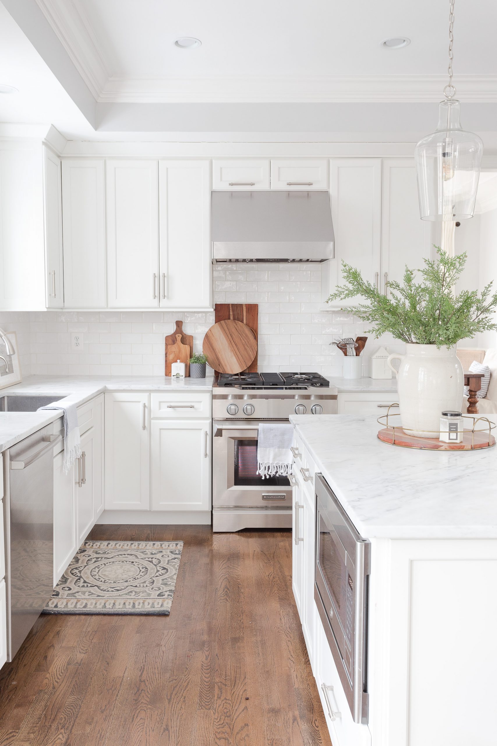 White kitchen with dark hardwood floors, marble countertops, white subway tile and stainless steel gas range.