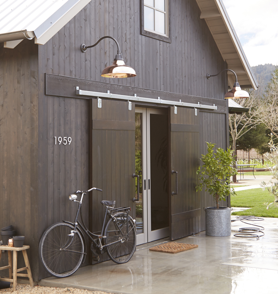 black barn with copper gooseneck lights, potted tree by the door and a bicycle propped up next to the building