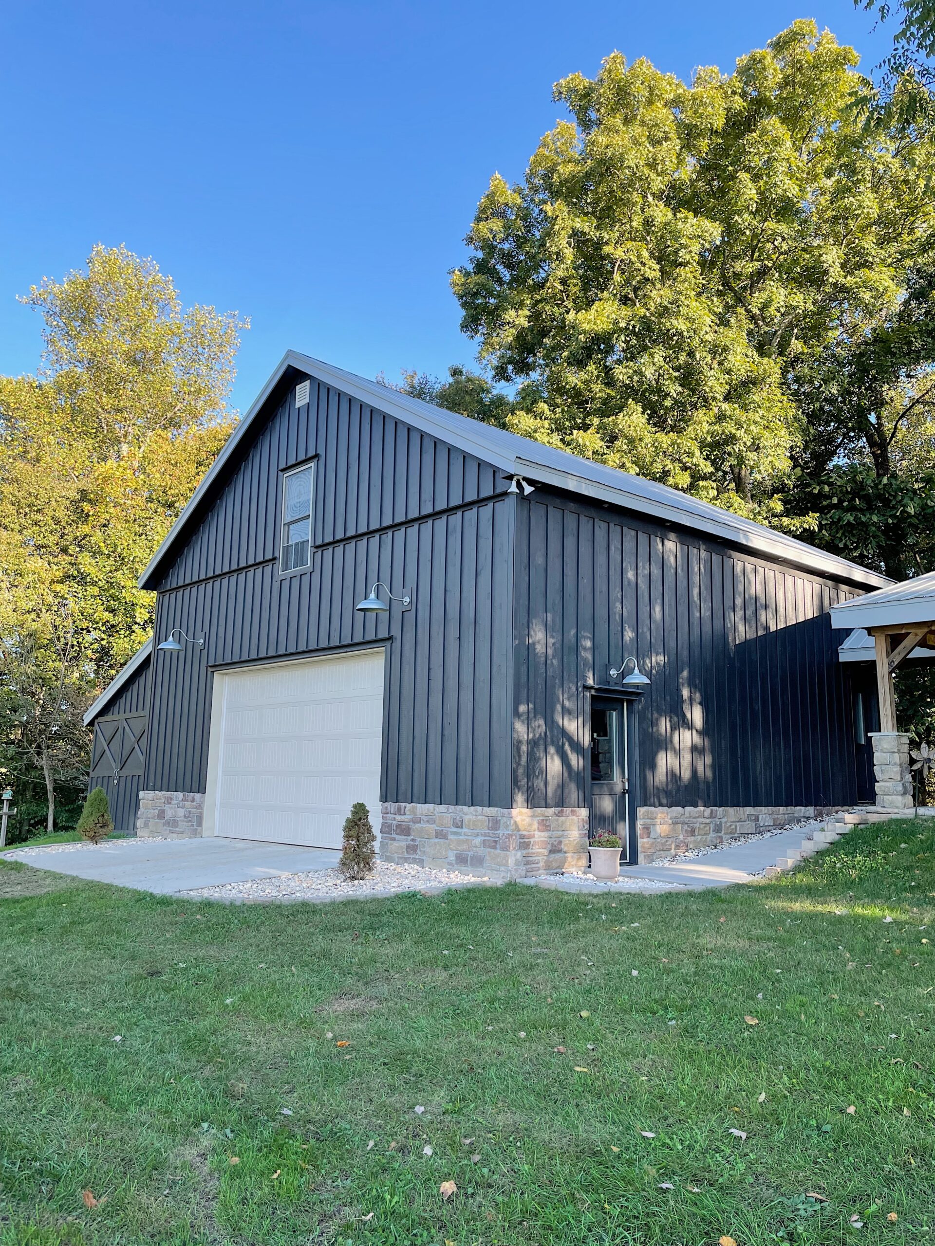 Black barn with stone foundation, two car garage and gray metal roof surrounded by trees