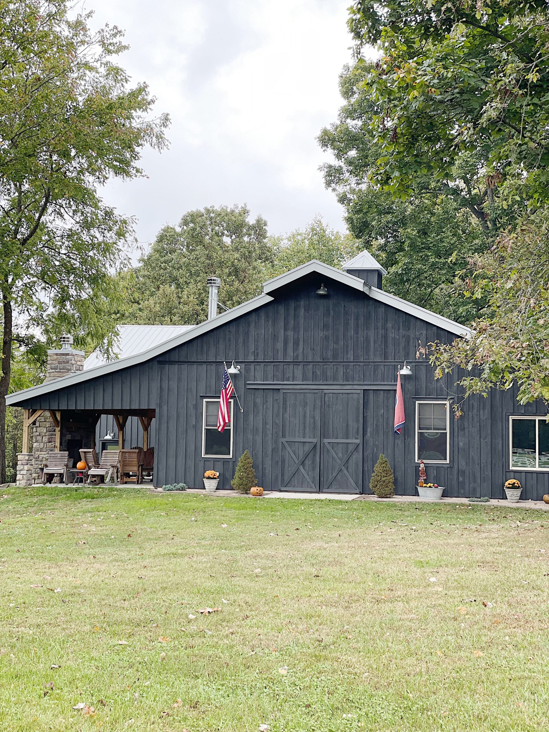 Black painted barn with gray roof and flags on either side of barn doors 