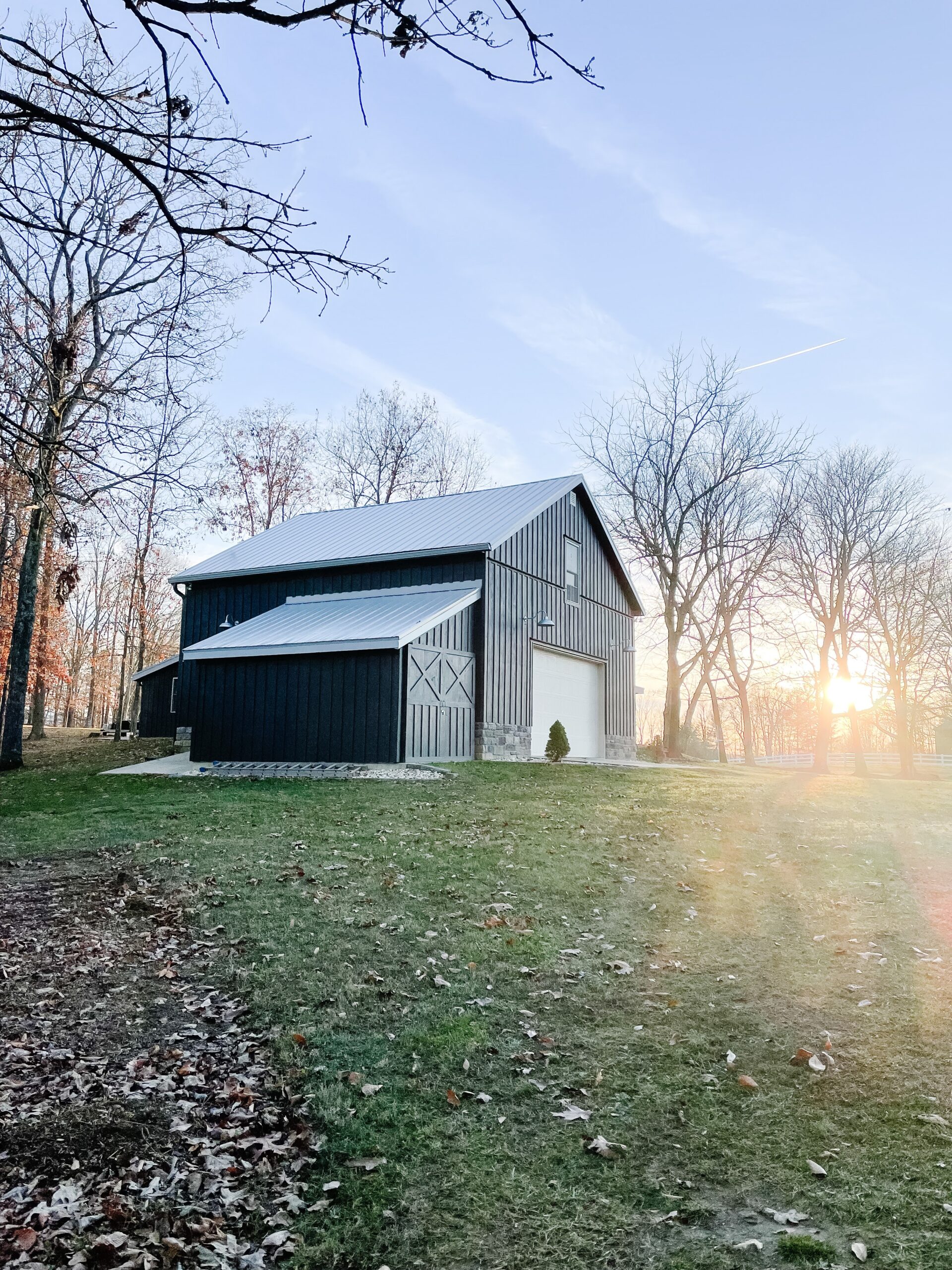 Black Barn with garage door on a winter day with sun setting next to the barn
