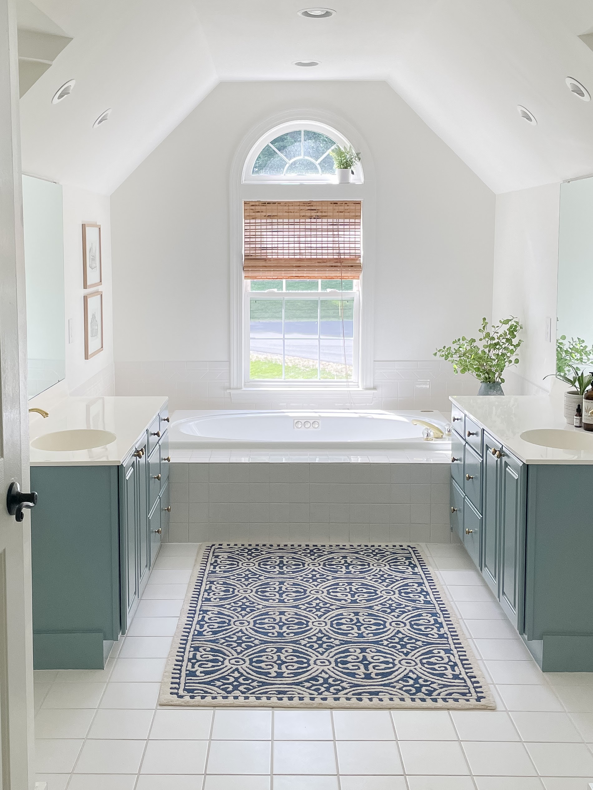 White bathroom with paint thermofoil bathroom cabinets with blue paint, rug and vase of greenery