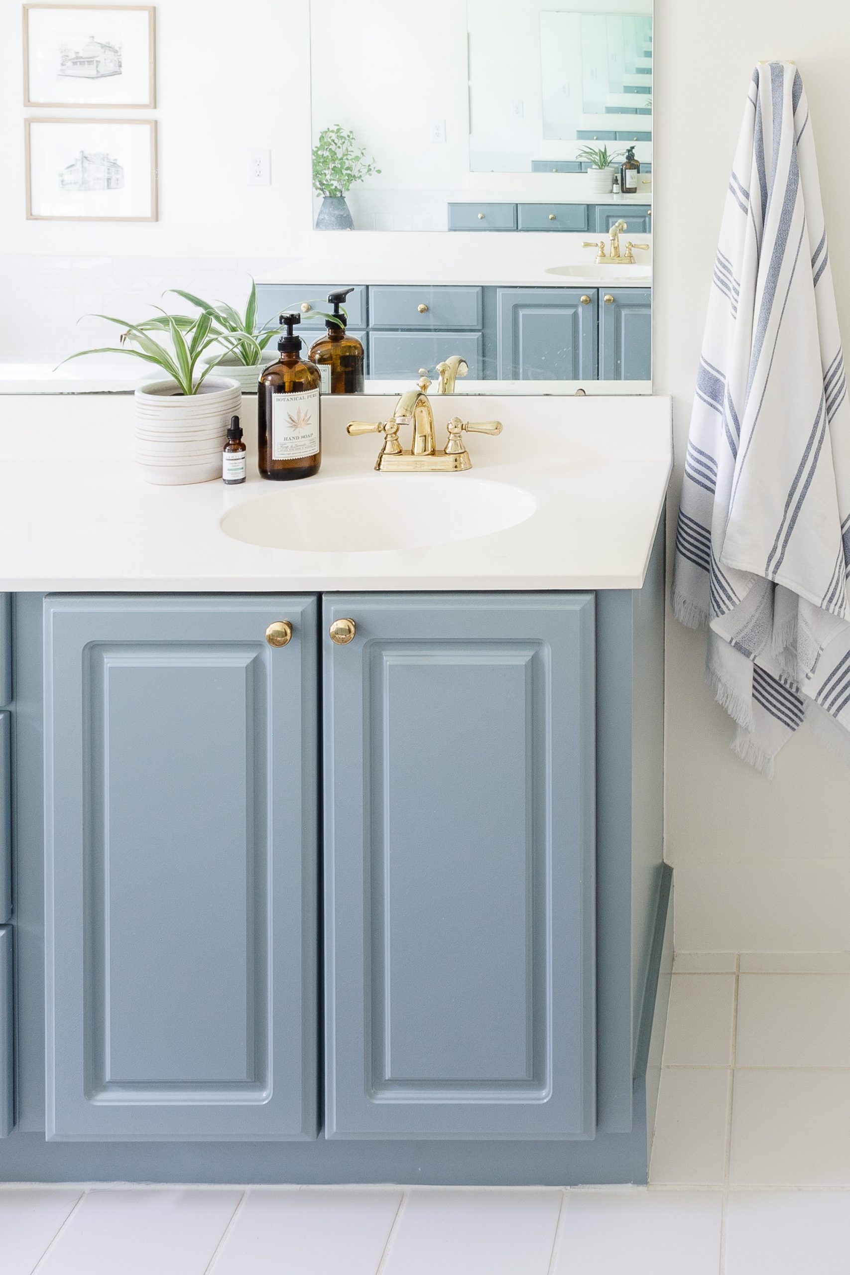 blue painted bathroom cabinet in white bathroom with blue and white stripe towel hanging on the wall and gold faucet