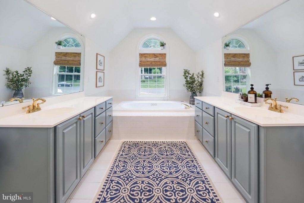 white bathroom with blue painted bathroom cabinets and window above tub. 