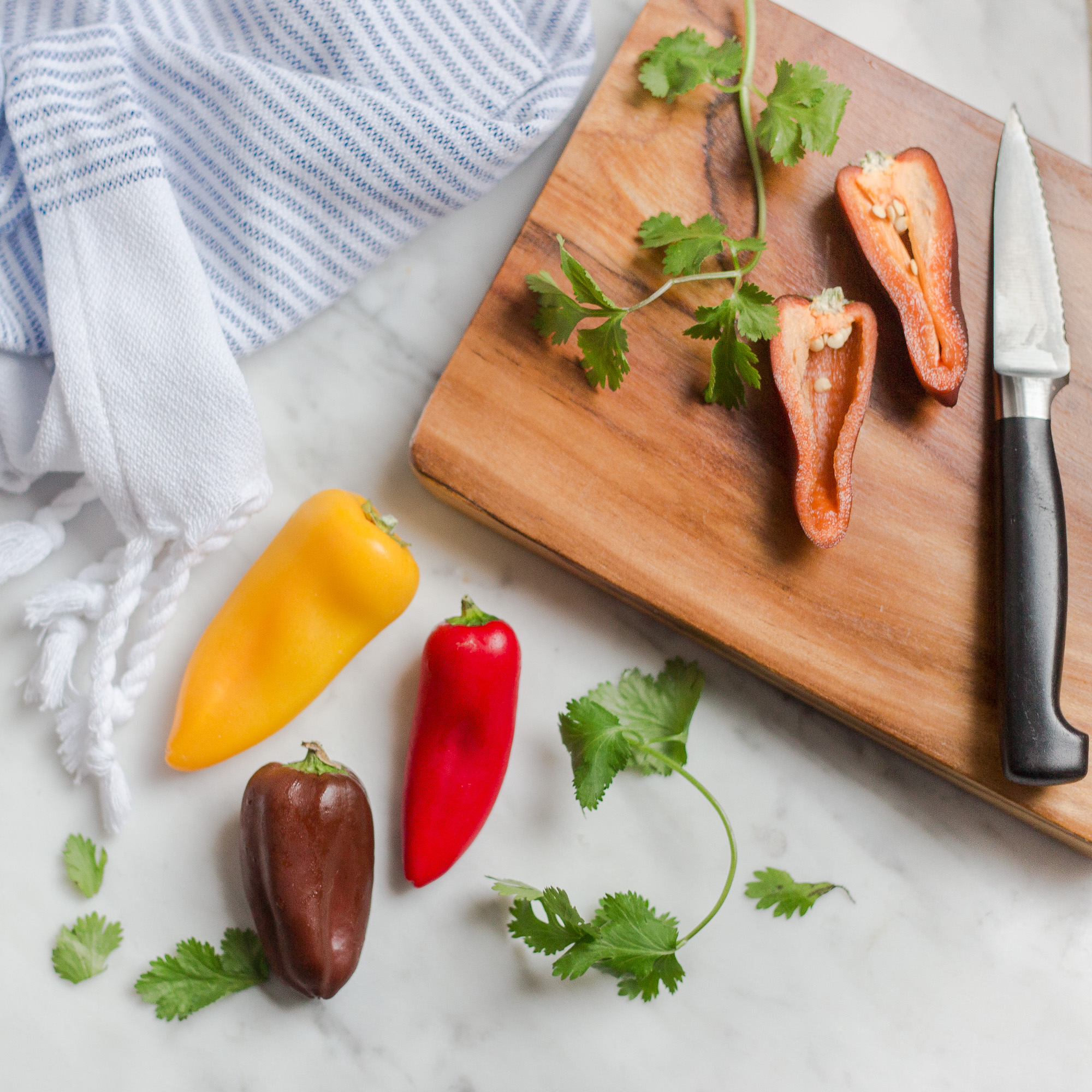 wooden cutting board with knife and bells peppers cut open and blue and white stripe towel sitting next to board