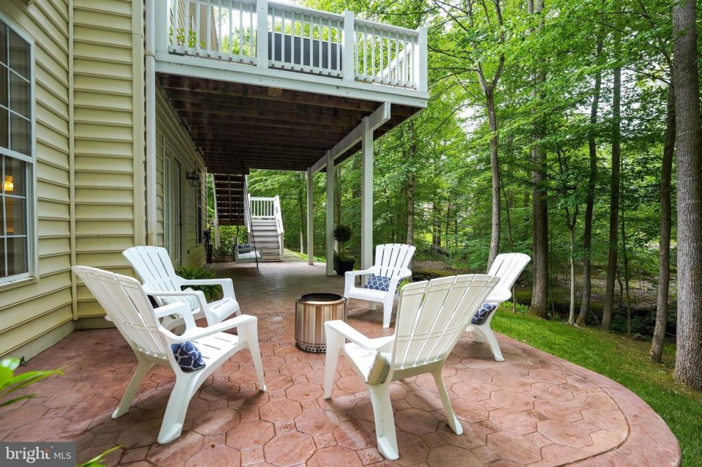 white patio chairs around fire pit sitting on patio overlooking the woods. 