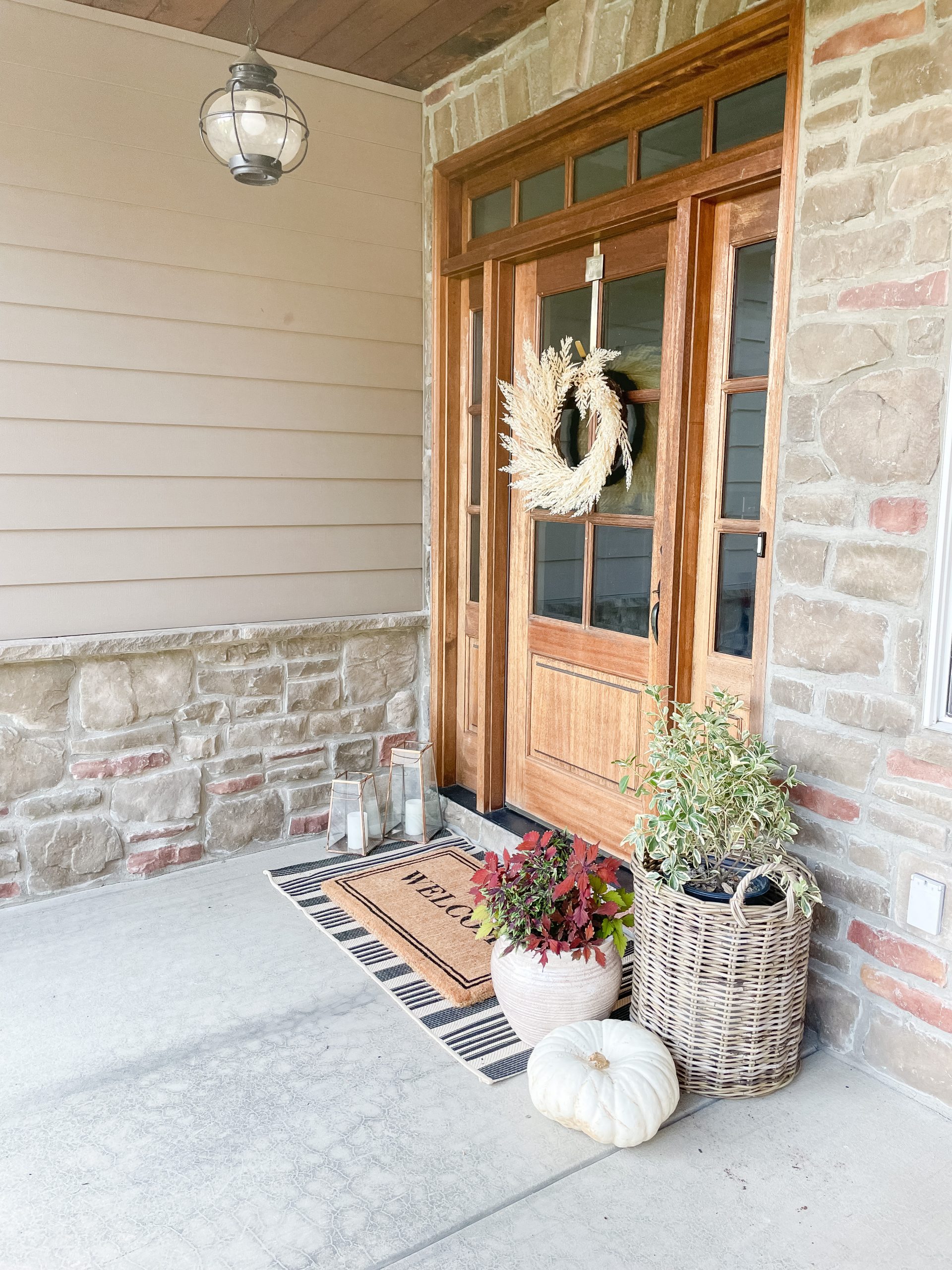 front wood door with basket filled with green busy, white pumpkin and welcome mat