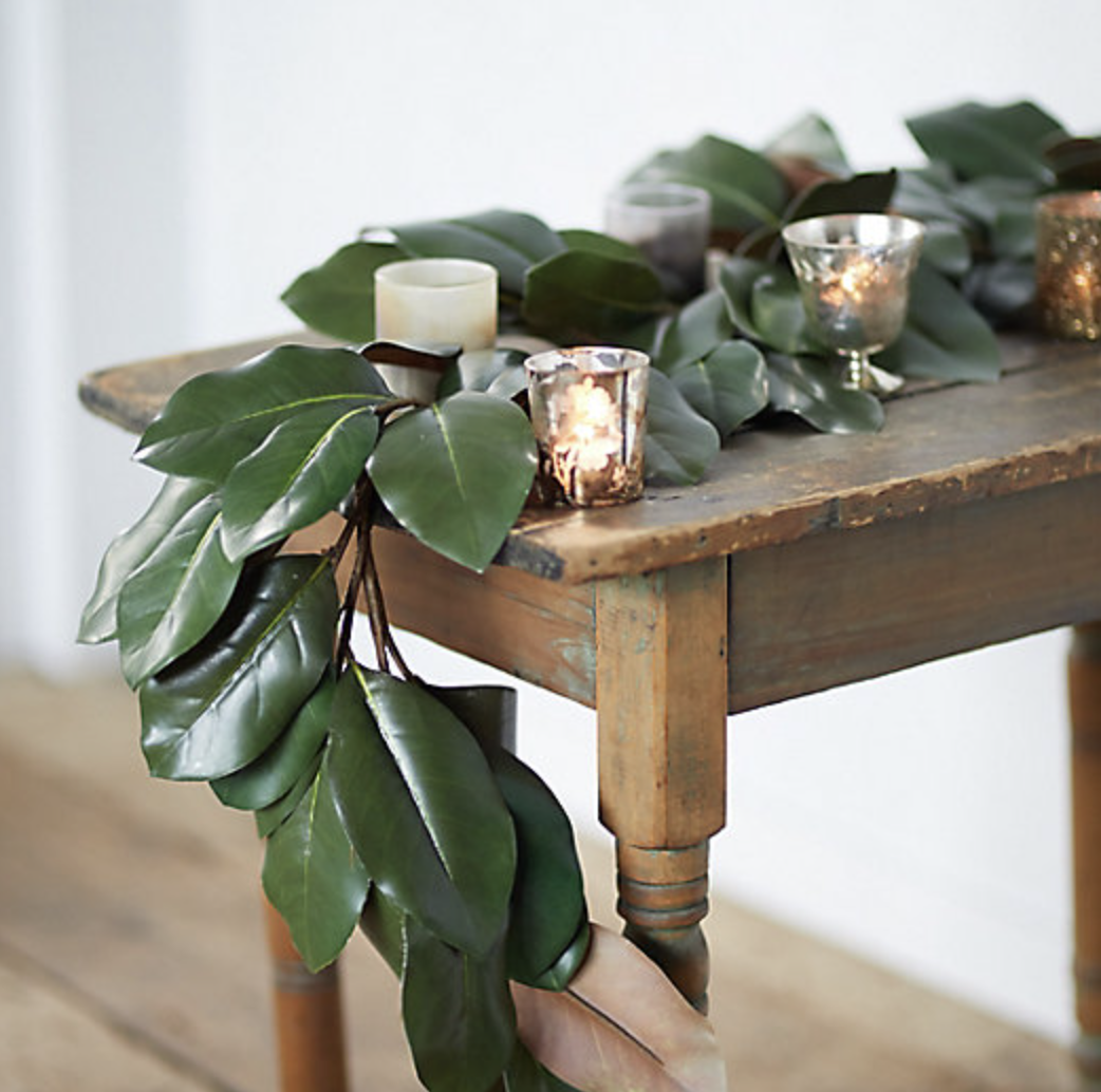 magnolia garland draped on wood table with mercury glass candles
