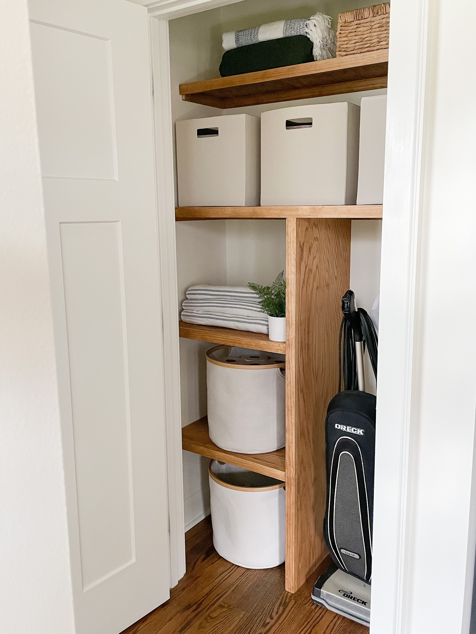 wood shelves in closet with storage bins, towels and vacuum. 