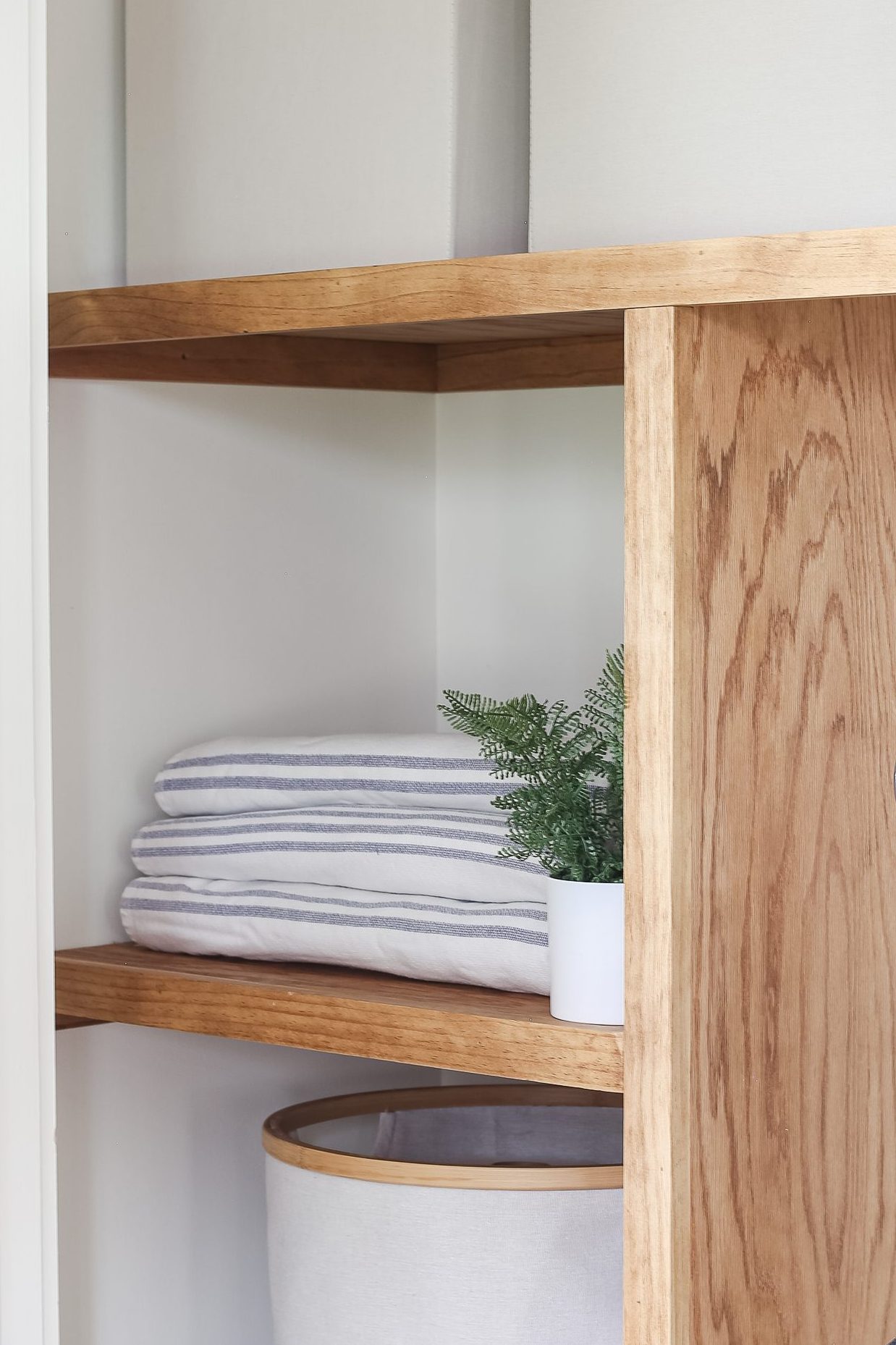 wood shelves in closet with storage bins, towels and vacuum. 