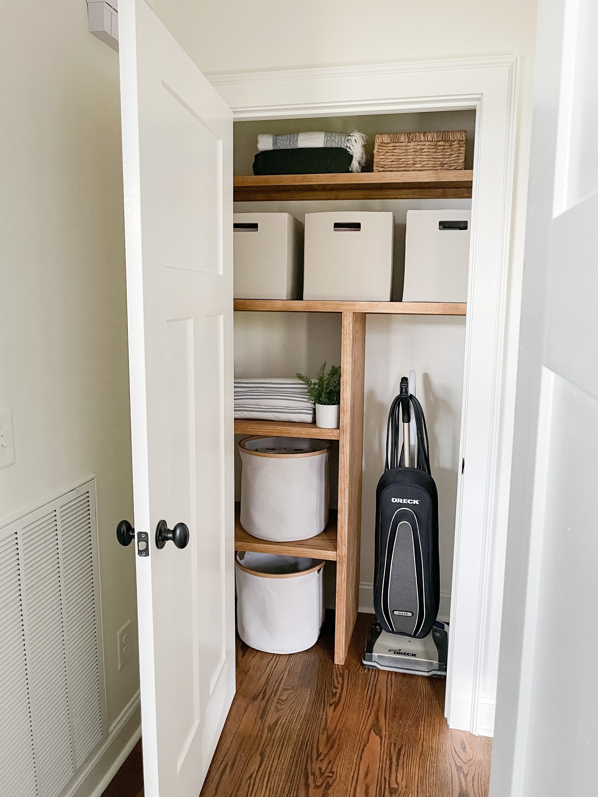 open door to closet with Wood Shelves, towel on shelf, vacuum against the wall and storage bins