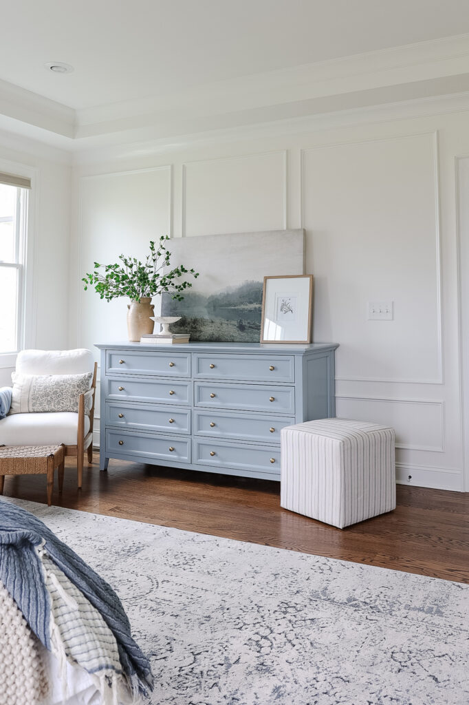 blue dresser with picture frame moulding, chair and vase of greenery on top of dresser with artwork