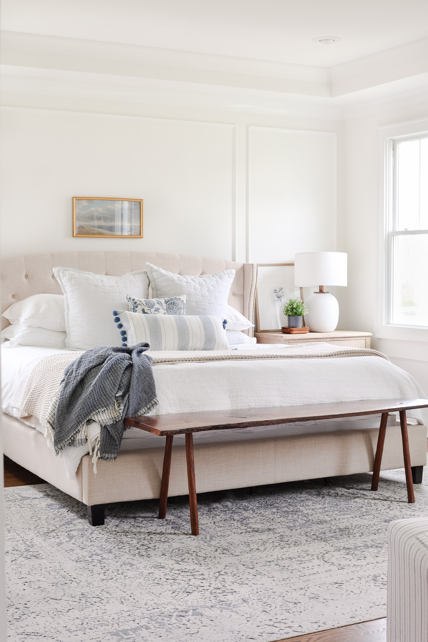 upholstered bed with white and blue bedding with bench and picture above the bed