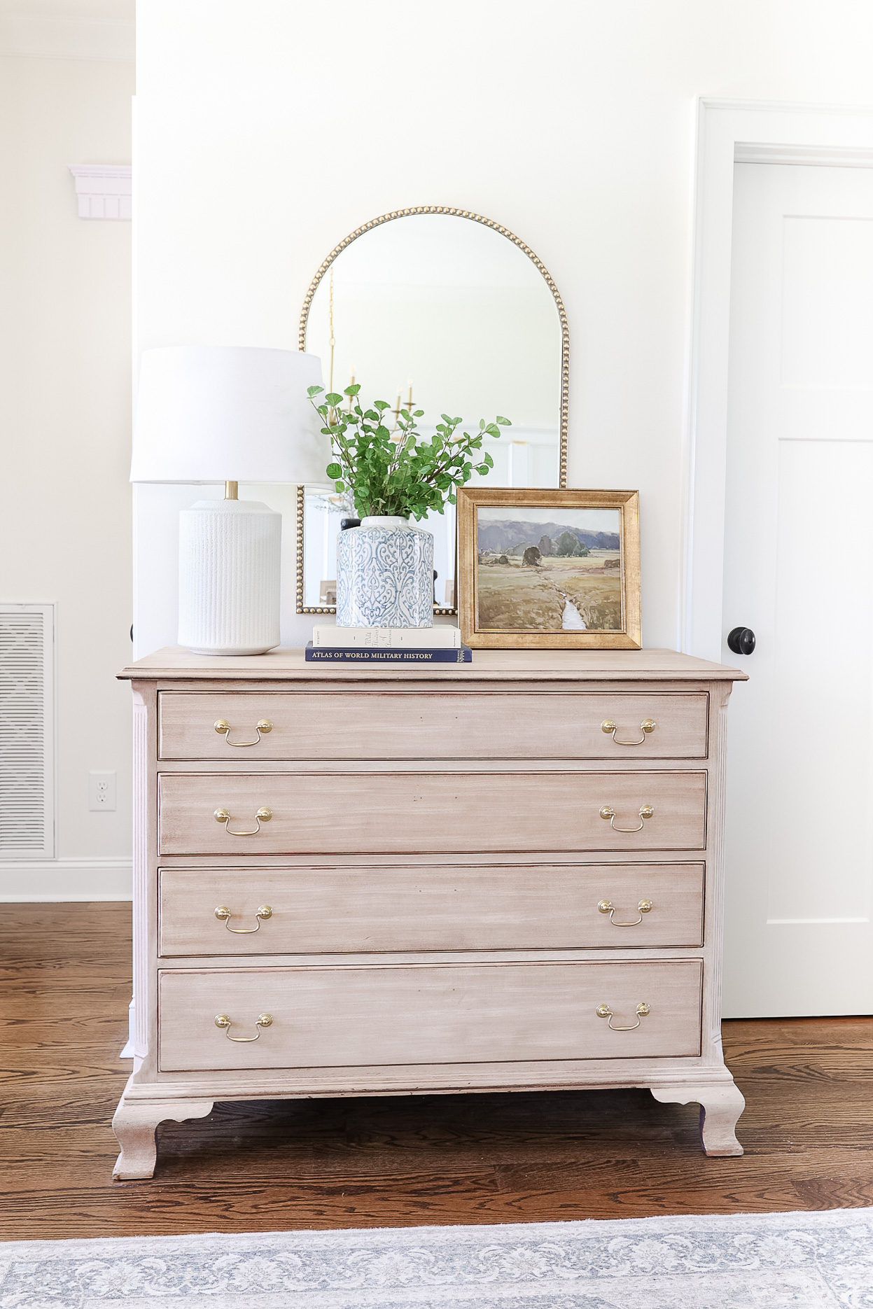 light wood dresser in hallway with arched mirror, vase of greenery and white lamp