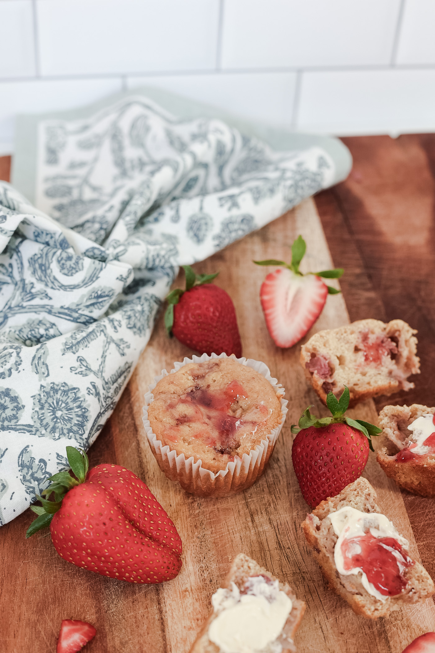 Strawberries and strawberry muffins on a wooden cutting board with white and blue floral napkin