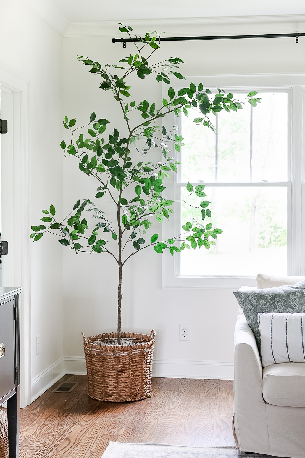 fake tree in living room sitting in basket next to window