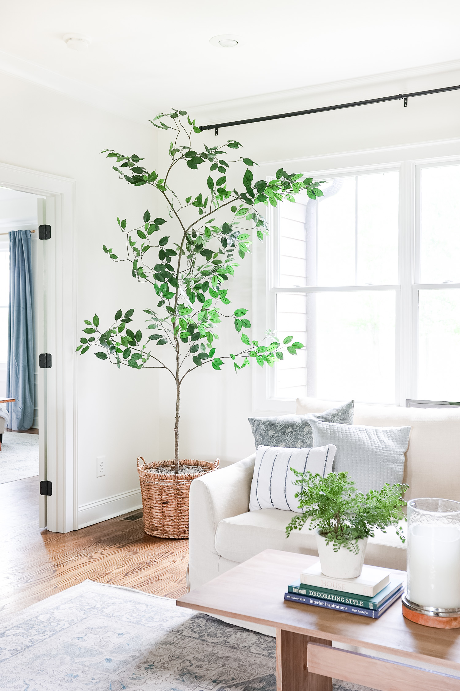 fake tree in living room sitting in basket next to window