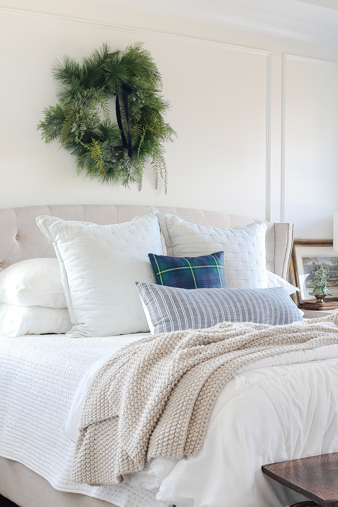 bed with white bedding, blanket, pillows and christmas wreath above bed
