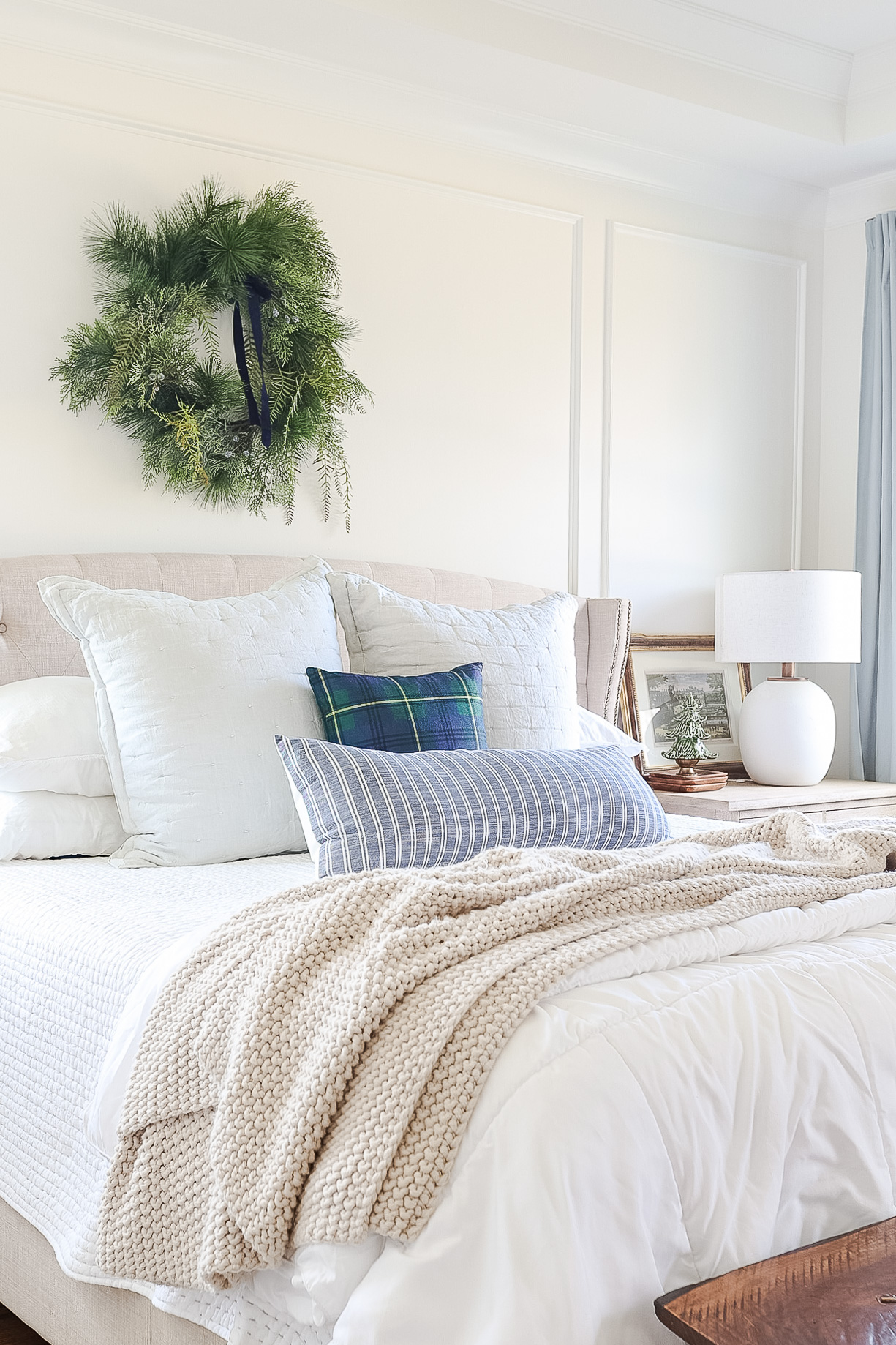 bed with white bedding, blanket, pillows and christmas wreath above bed