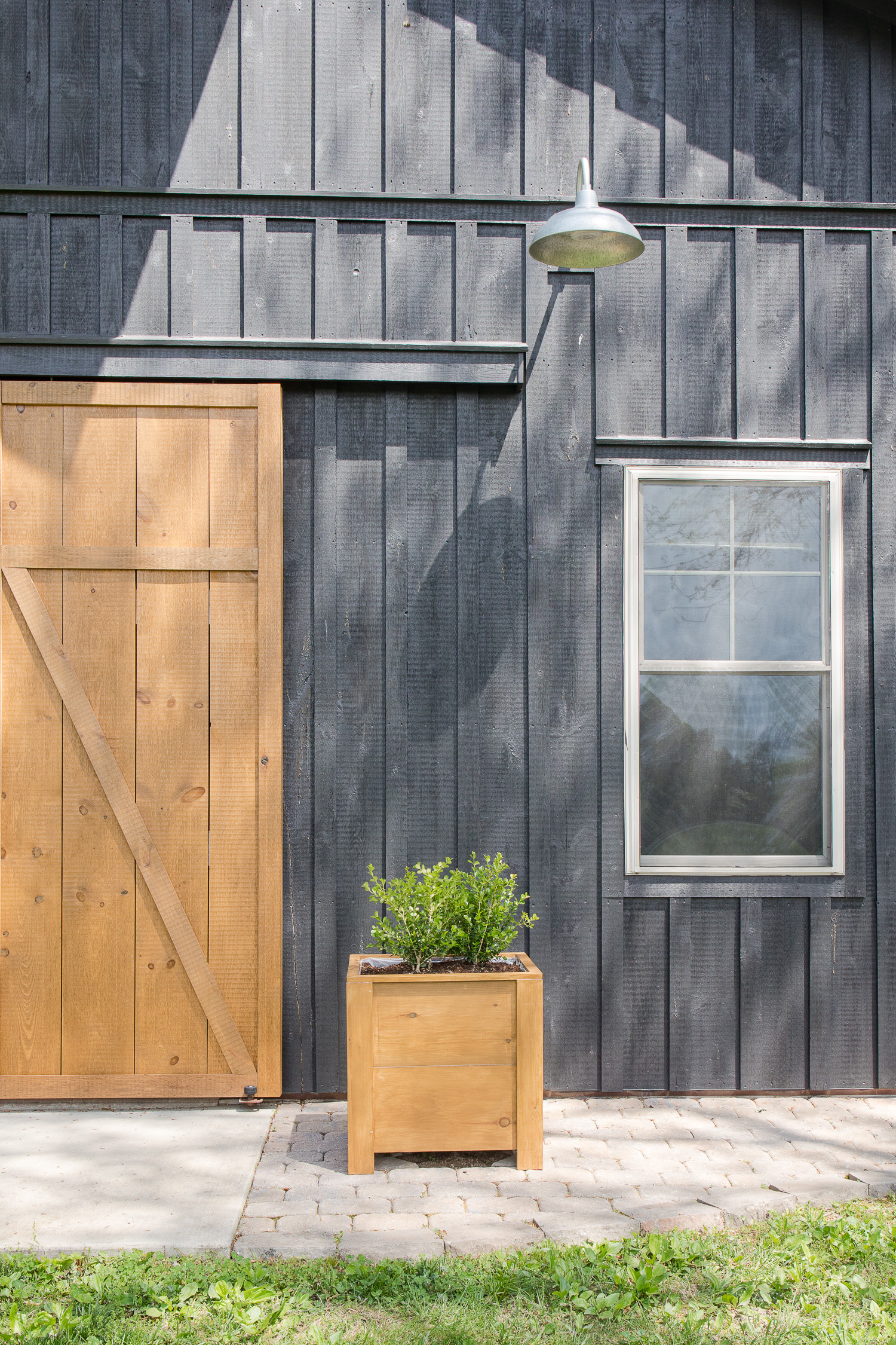 black barndominium with wood doors and wooden planters with boxwoods in front