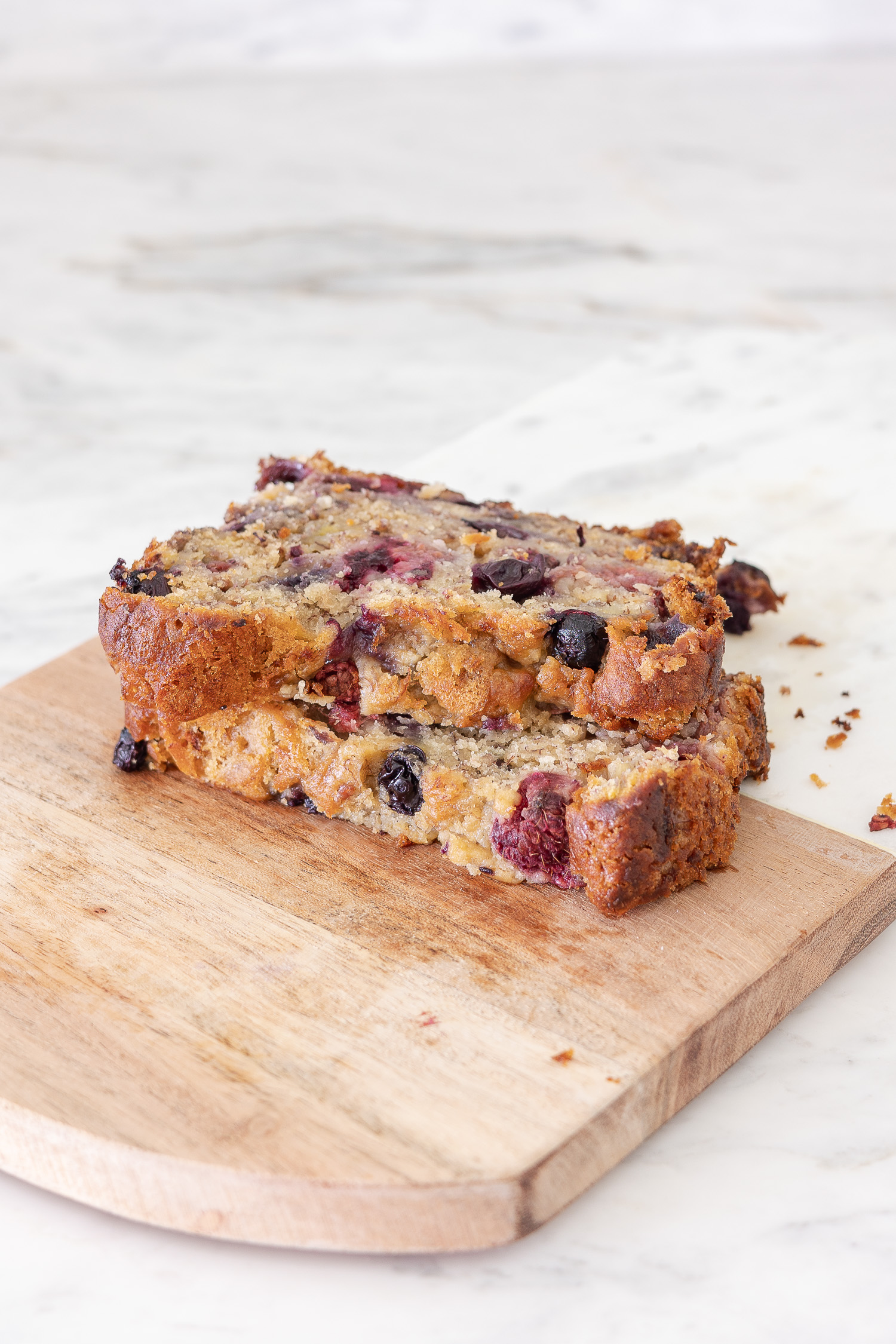 berry banana bread sitting on wood tray on marble countertop