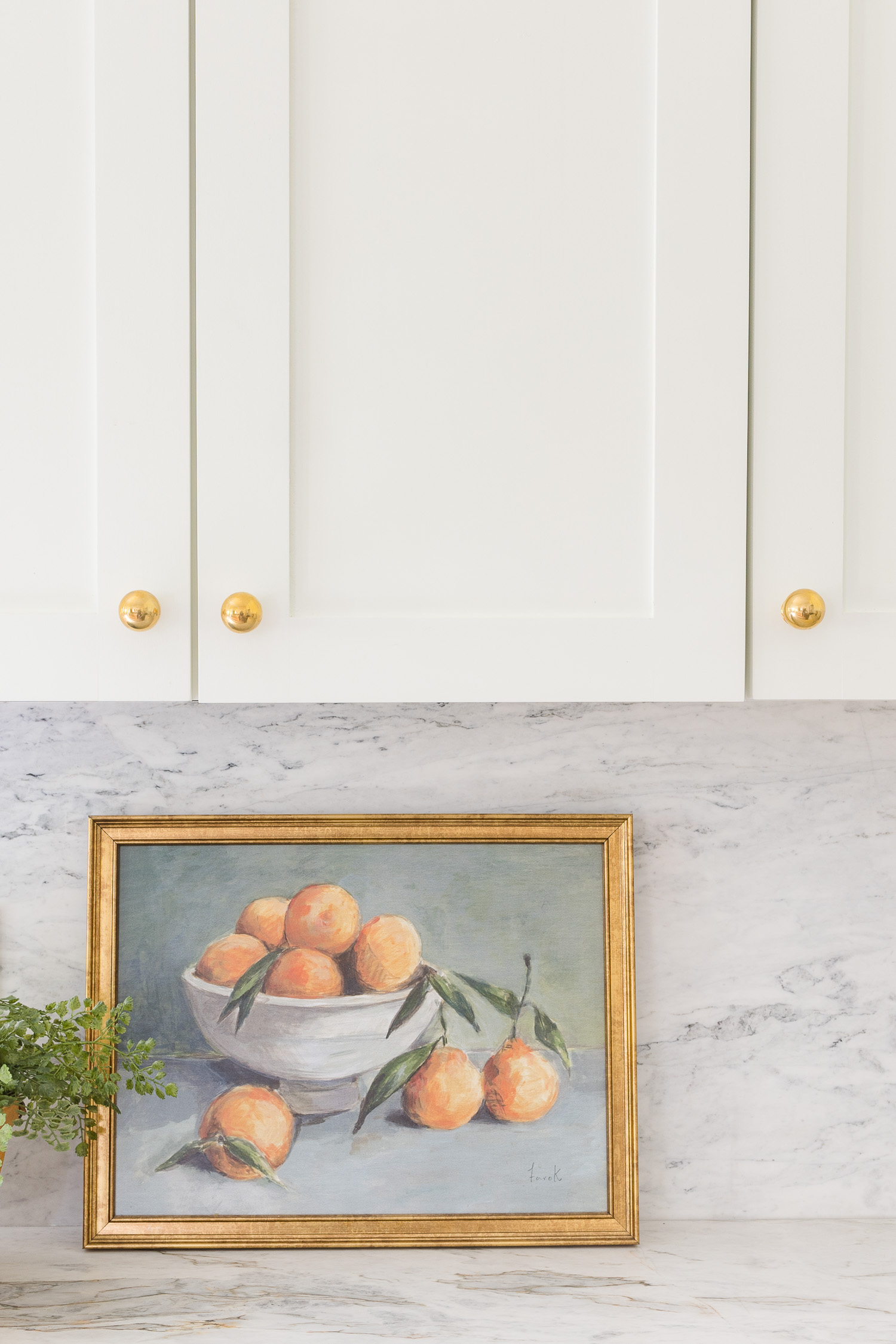 white kitchen with brass knob hardware and painting on counter