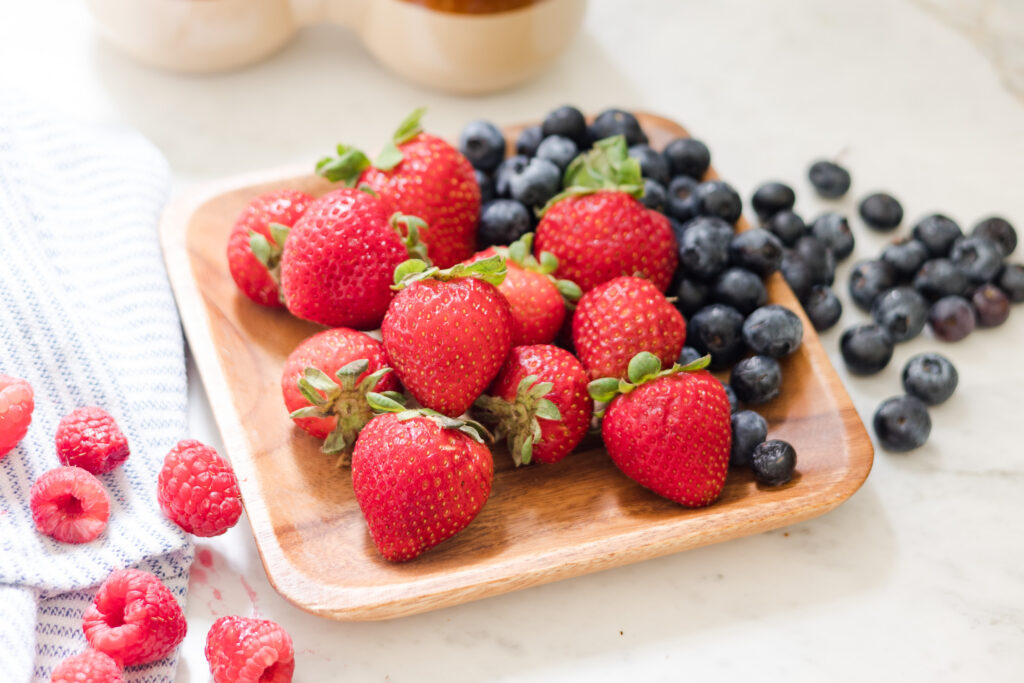 wood tray of strawberries with blueberries and raspberries
