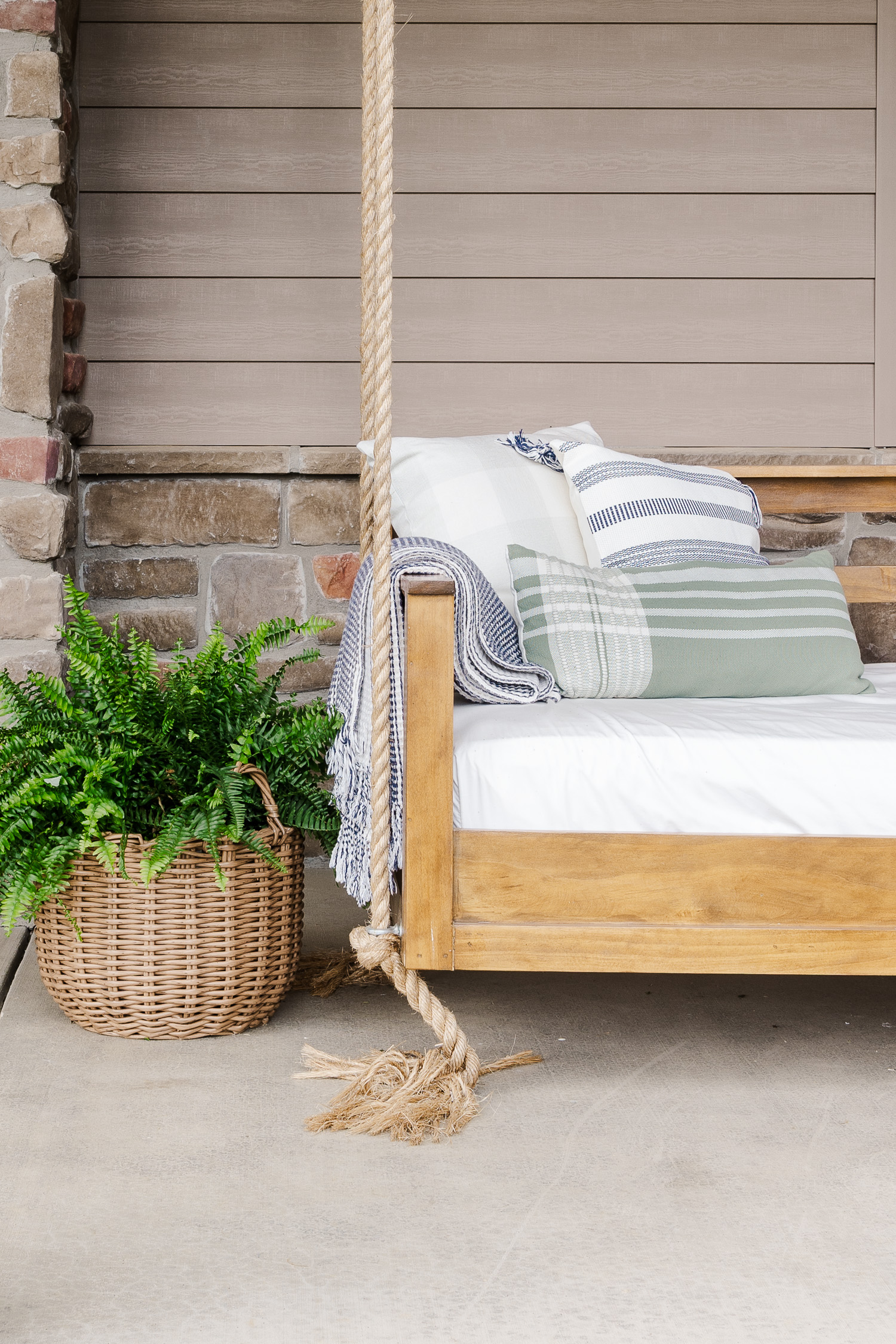 wood patio swing bed with fern in basket and pillows and blanket on swing